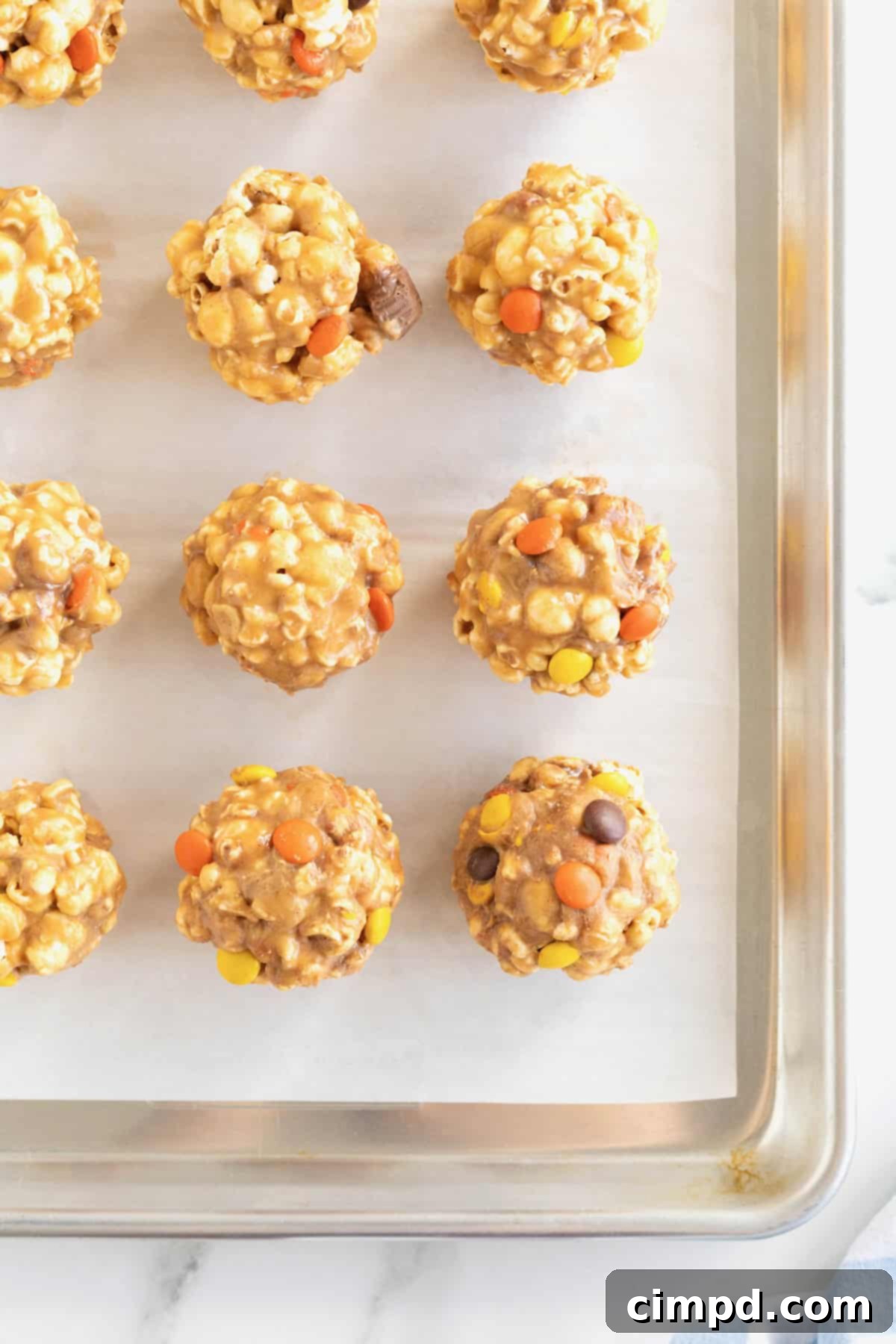 12 peanut butter popcorn balls on a parchment lined aluminum baking tray.