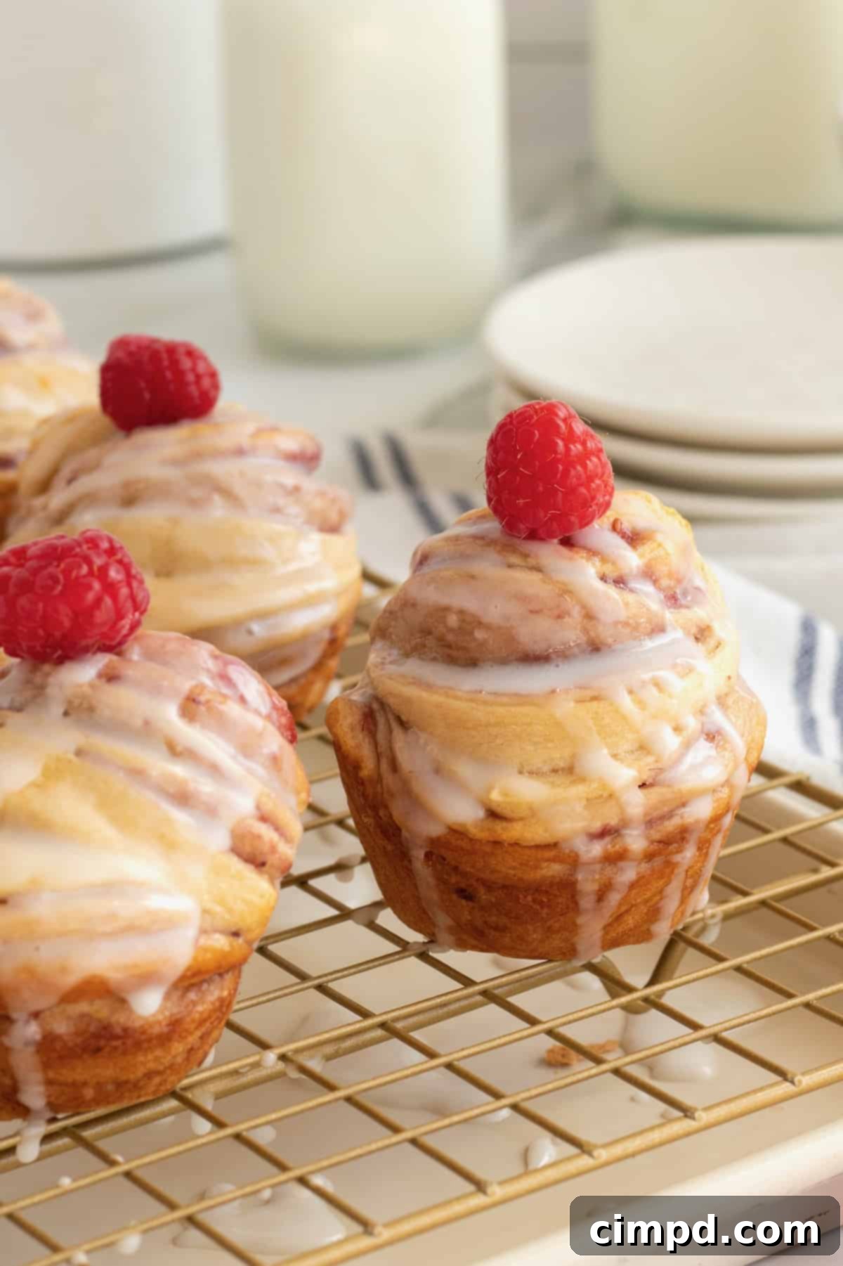 Cruffins topped with glaze and a fresh raspberry on a cooling rack, showcasing their golden-brown perfection.