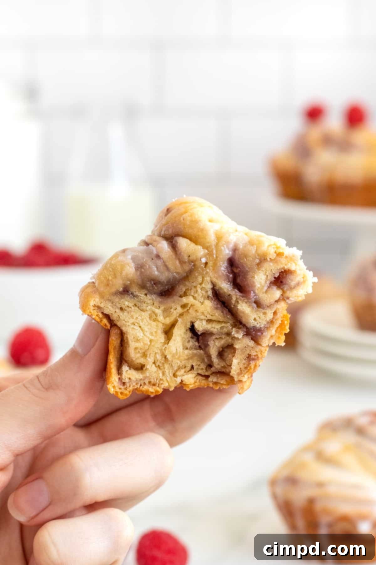 A cross-section of a Raspberry Cream Cheese Cruffin, revealing layers of flaky pastry, raspberry preserves, and cream cheese filling, all topped with a sweet glaze.
