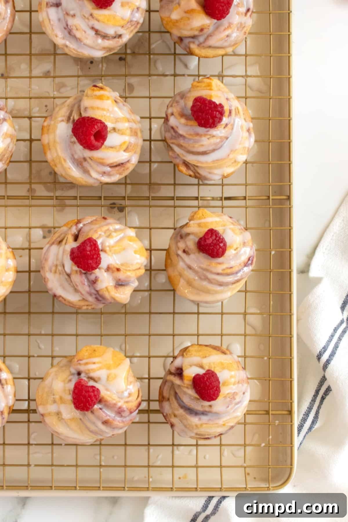 A collection of freshly baked Raspberry Cream Cheese Cruffins, each beautifully glazed and topped with a fresh raspberry, arranged on a cooling rack.