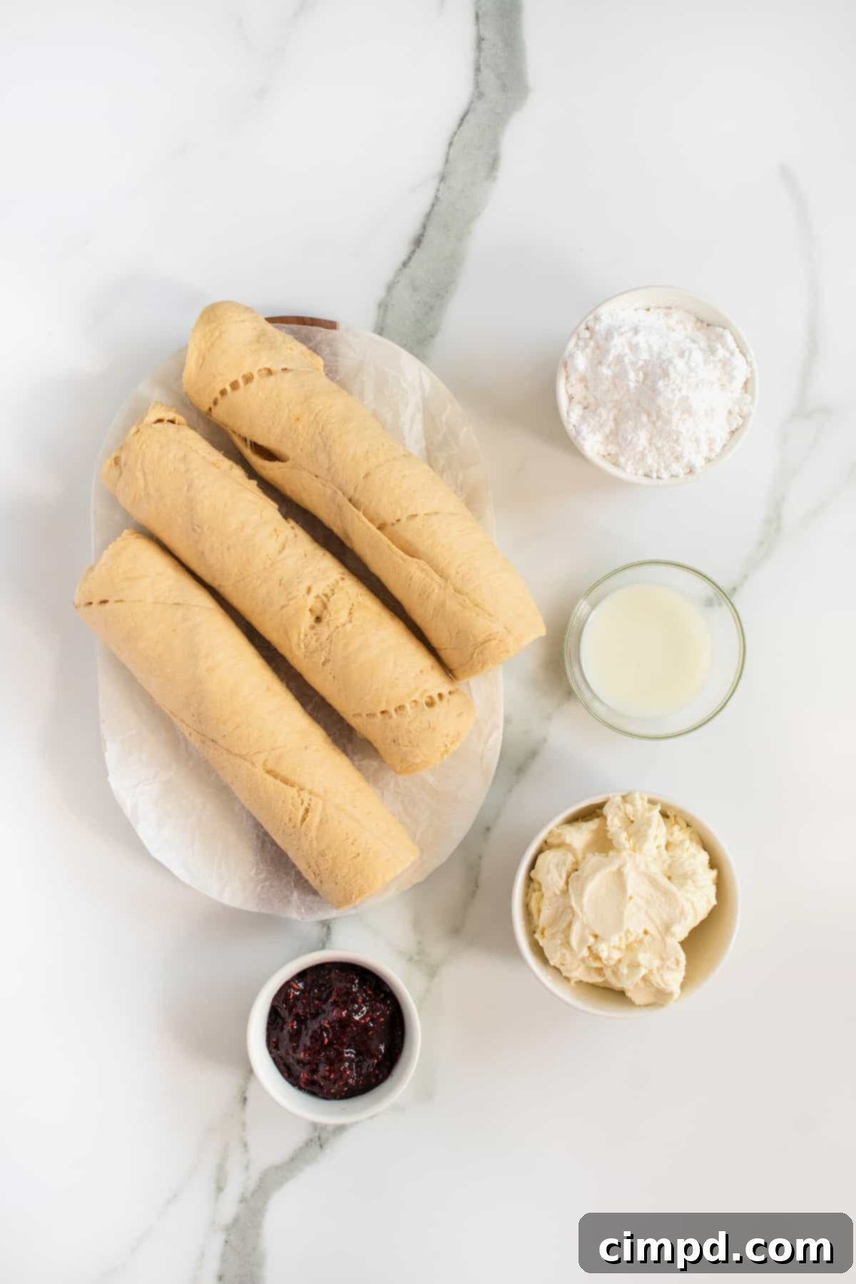 All the ingredients for Raspberry Cream Cheese Cruffins laid out on a kitchen surface, including crescent roll dough, cream cheese, raspberry preserves, powdered sugar, and milk.