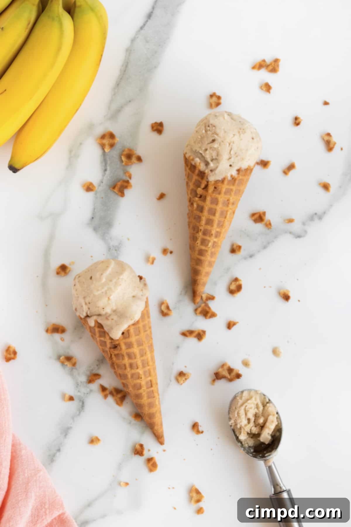 Pure Banana Bliss 6 A hand holding a scoop of One-Ingredient Banana Ice Cream in a cone, with more ice cream in a bowl in the background, by The BakerMama
