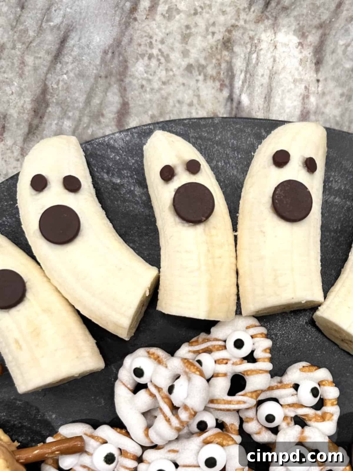 5 Spooktacularly Cute Halloween Goodies 5 A plate of spooky cute Banana Ghosts with chocolate chip eyes and mouths, displayed on a Halloween-themed platter.