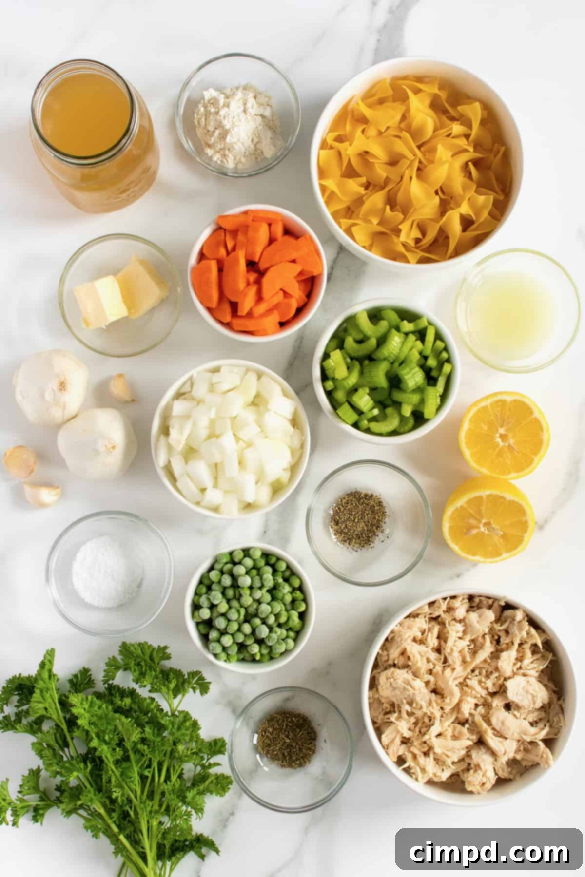 Ingredients laid out for homemade chicken noodle soup, including vegetables, chicken, and spices, by The BakerMama