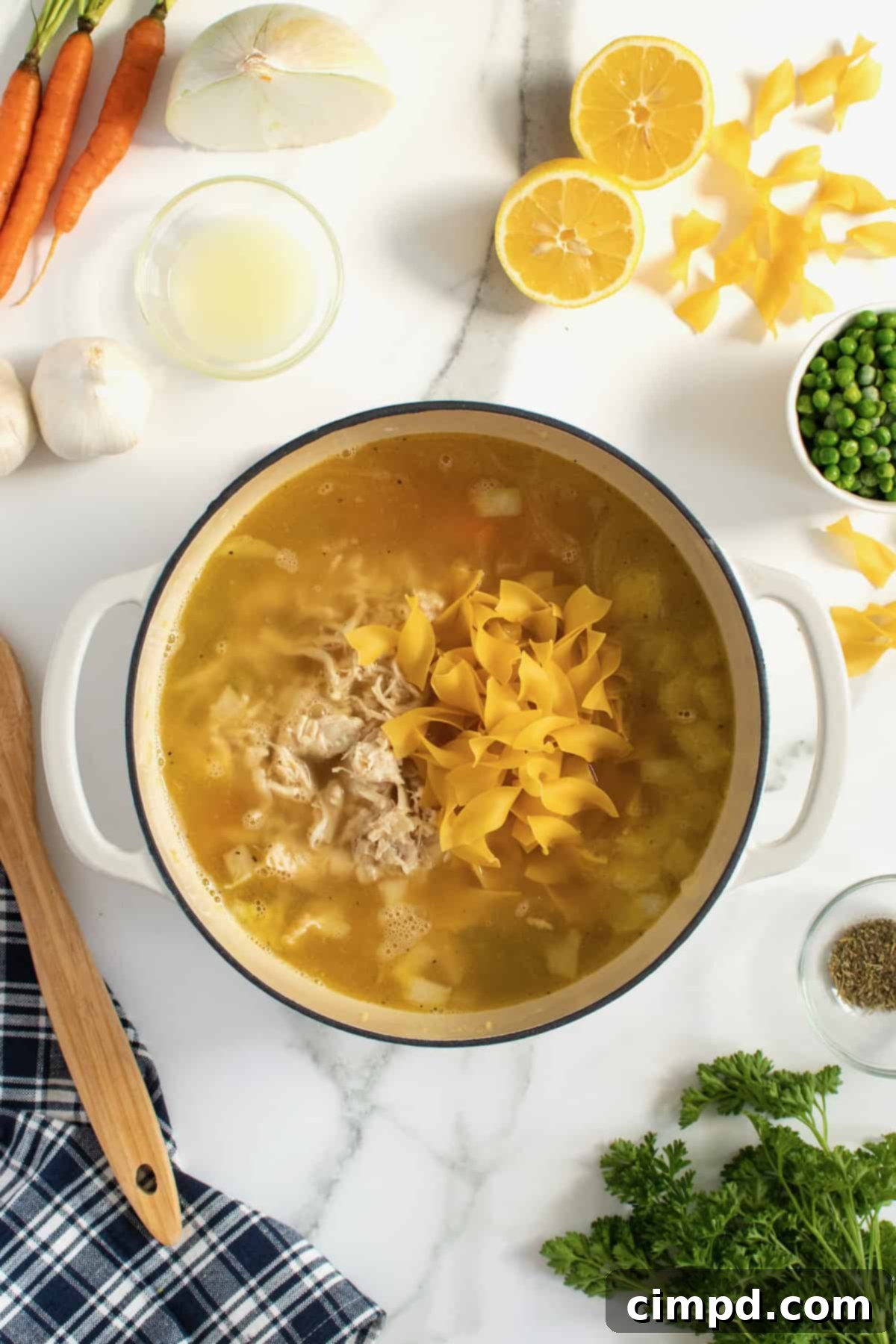 A pot of homemade chicken noodle soup with noodles and chicken simmering, by The BakerMama
