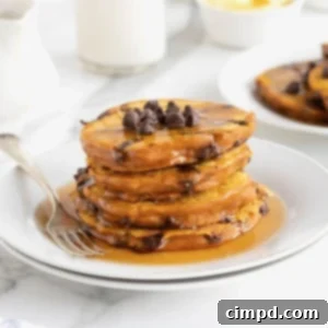 Spiced Pumpkin Chocolate Chip Pancakes 13 Four pumpkin chocolate chip pancakes stacked in a pool of syrup on a small white plate.