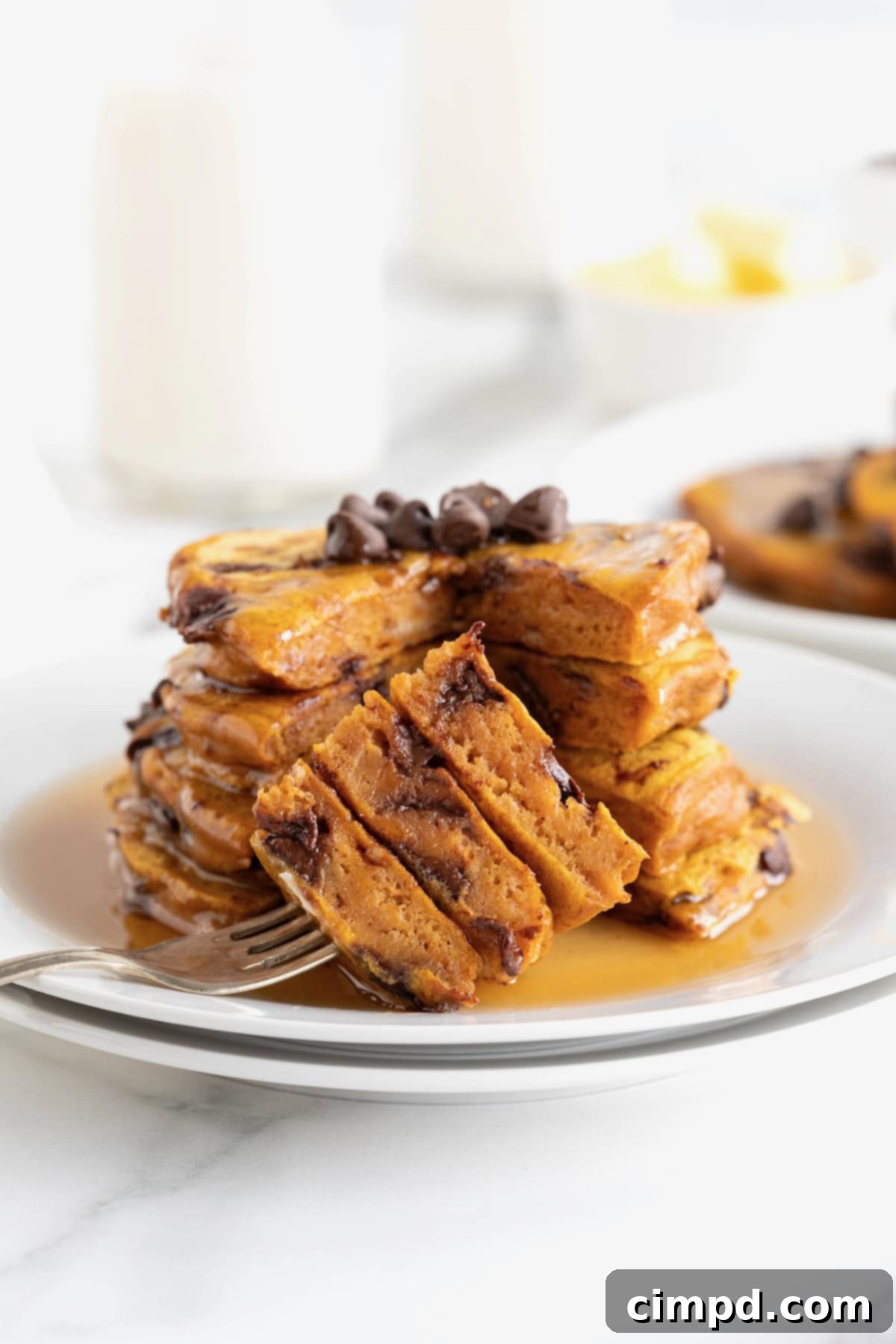 Spiced Pumpkin Chocolate Chip Pancakes 3 A stack of four golden-brown pumpkin chocolate chip pancakes bathed in a generous pool of maple syrup on a small white plate, with a fork holding a perfect bite.