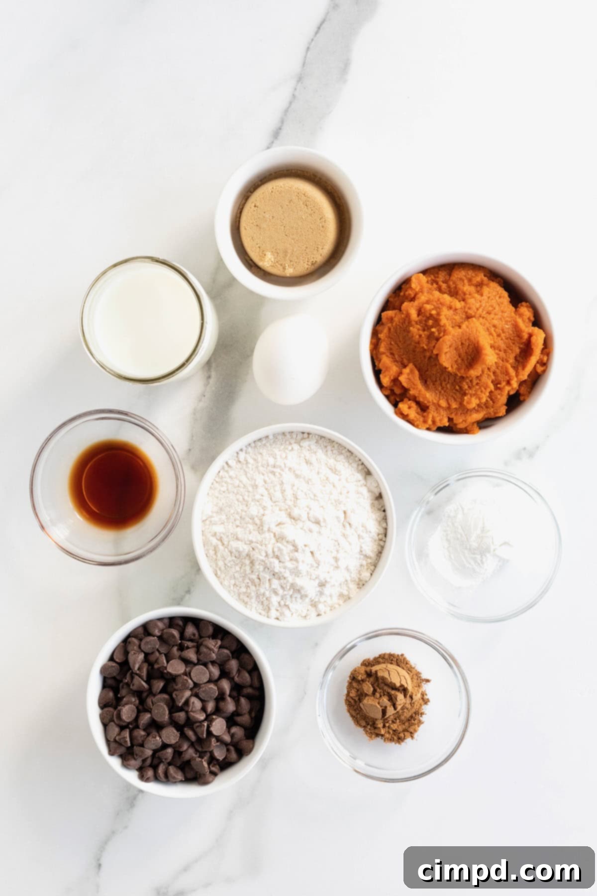 Spiced Pumpkin Chocolate Chip Pancakes 5 A beautifully arranged collection of ingredients for pumpkin chocolate chip pancakes, neatly placed in small glass containers on a pristine white marble countertop.