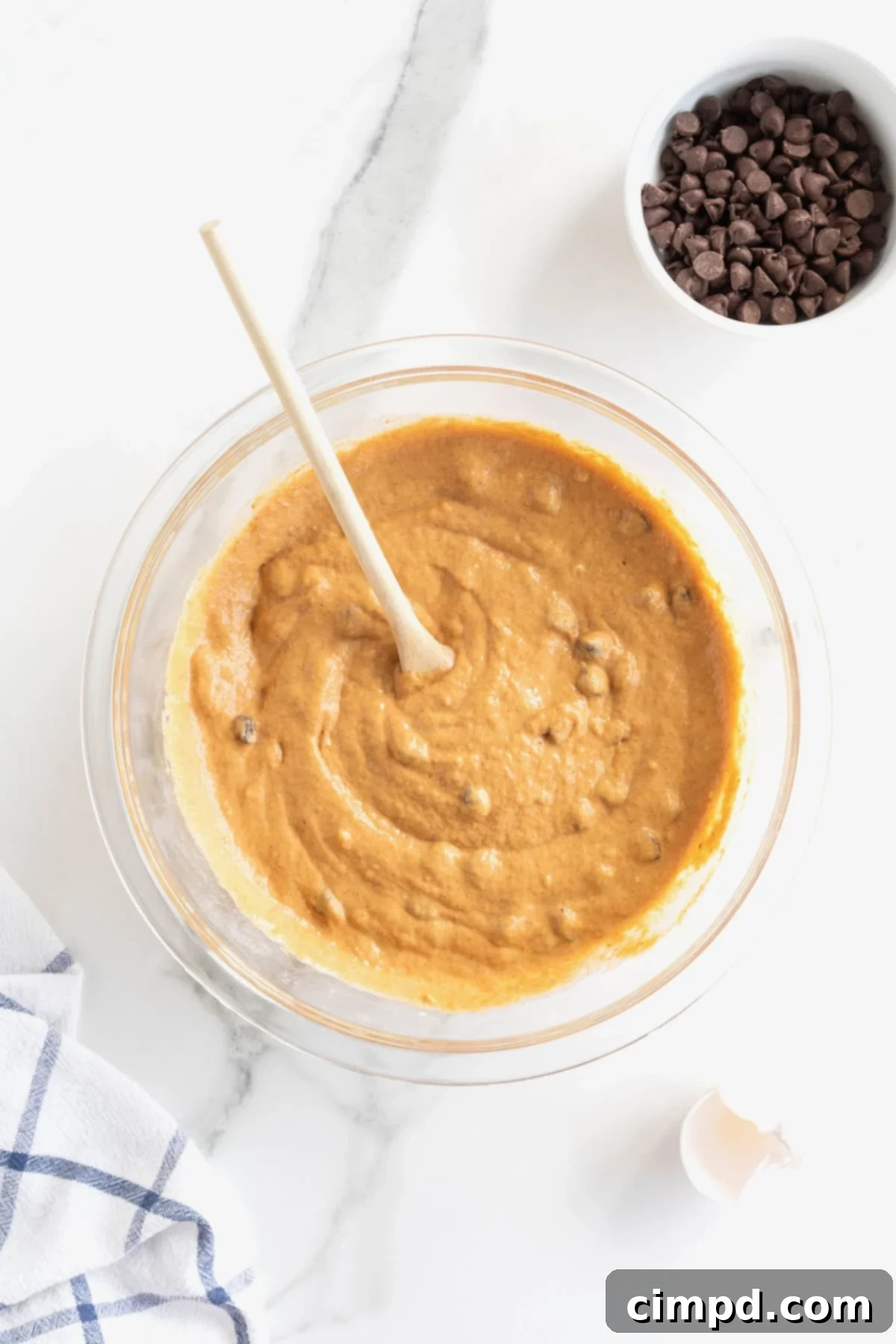 Spiced Pumpkin Chocolate Chip Pancakes 8 A large white bowl filled with creamy pumpkin chocolate chip pancake batter, featuring visible chocolate chips, with a wooden spoon resting inside.