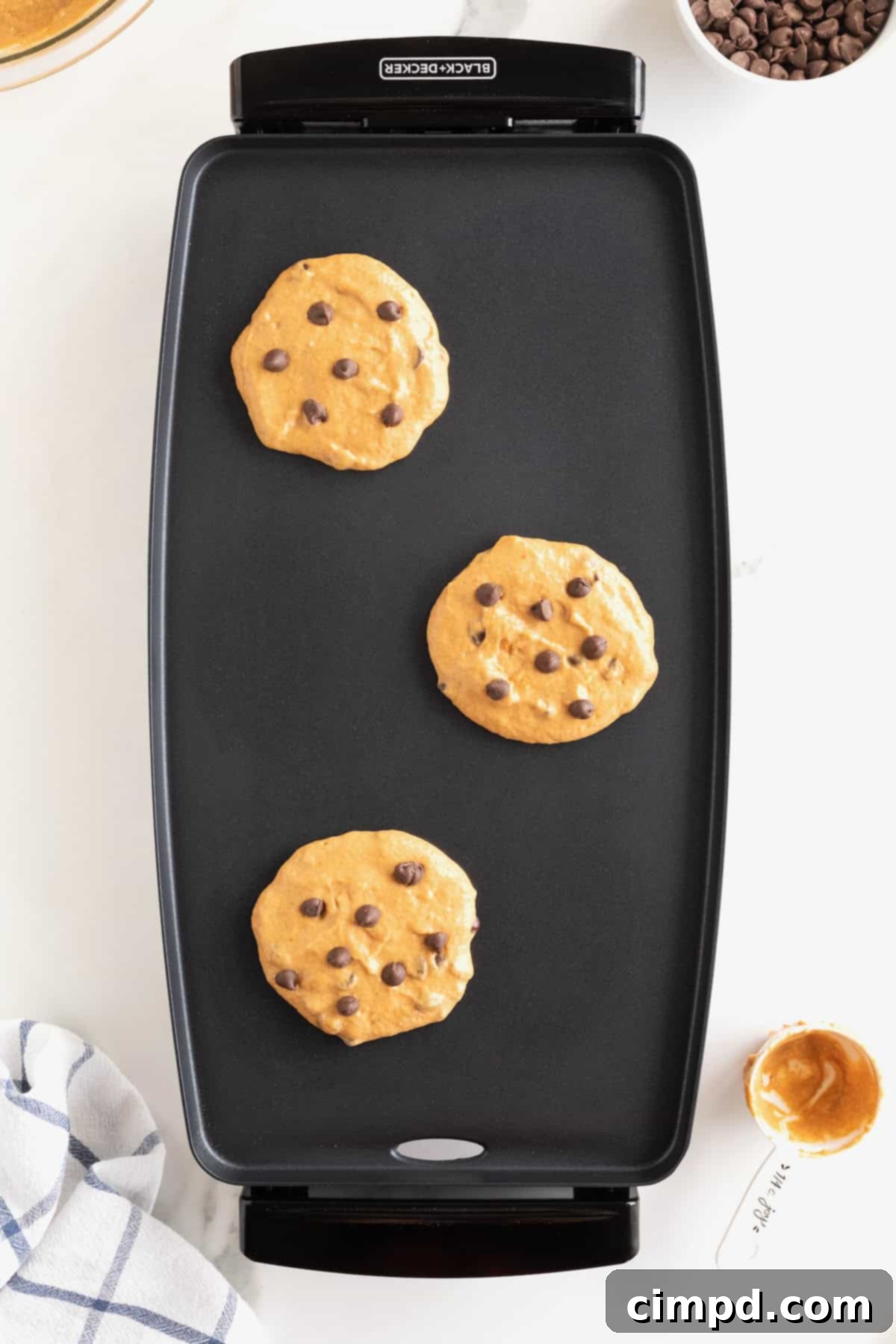 Spiced Pumpkin Chocolate Chip Pancakes 9 Three perfectly round pumpkin pancakes, golden brown and speckled with melting chocolate chips, cooking on a nonstick griddle.