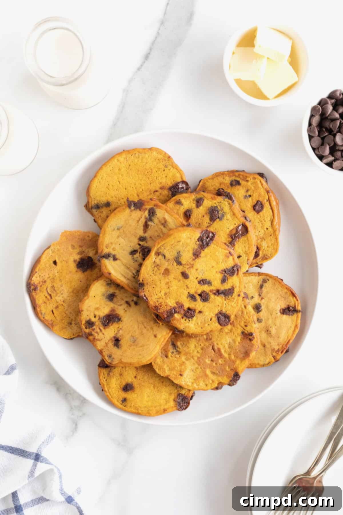 Spiced Pumpkin Chocolate Chip Pancakes 10 A large white serving plate piled high with a mouthwatering stack of golden-brown pumpkin chocolate chip pancakes, ready for a delicious breakfast.