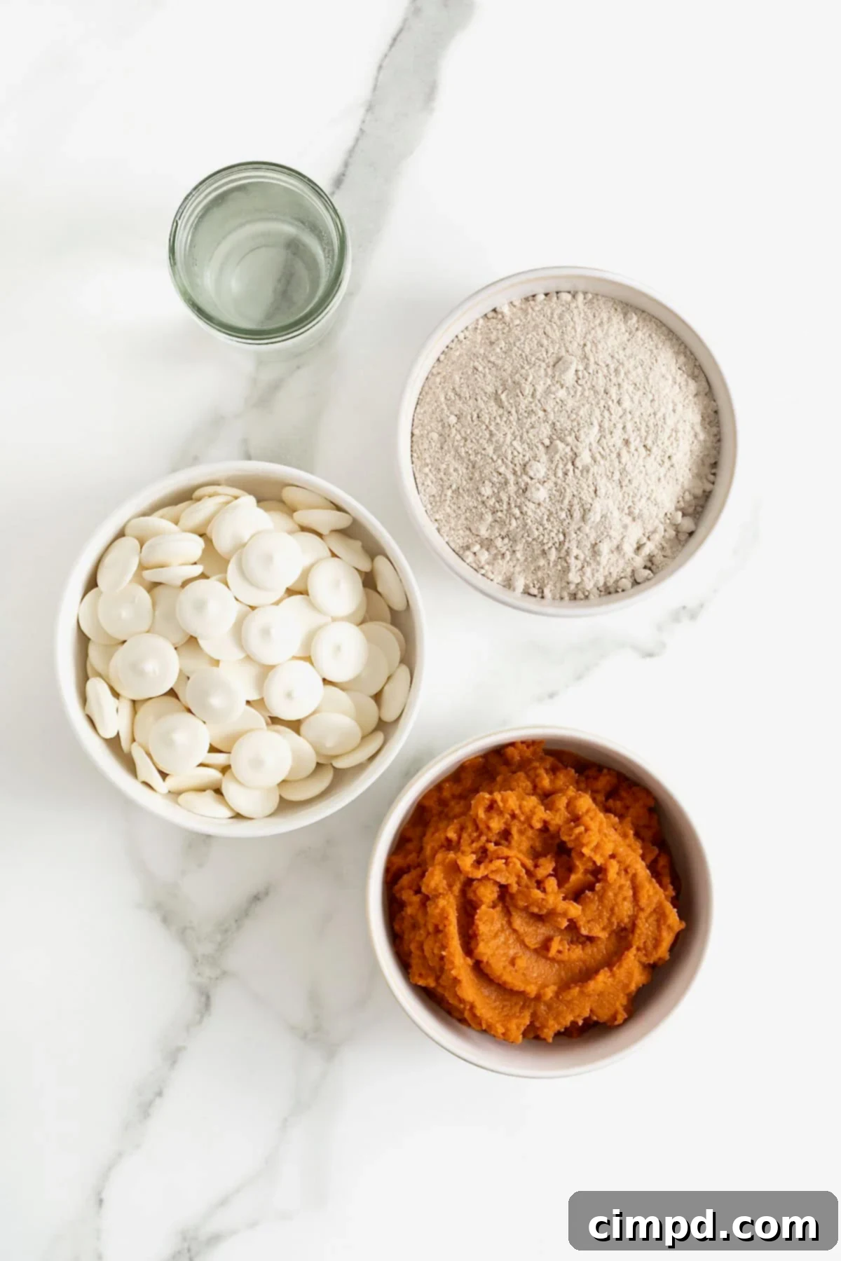 Ingredients for pumpkin spice cake balls, neatly arranged in white dishes on a white marble counter, showcasing the simple components needed.