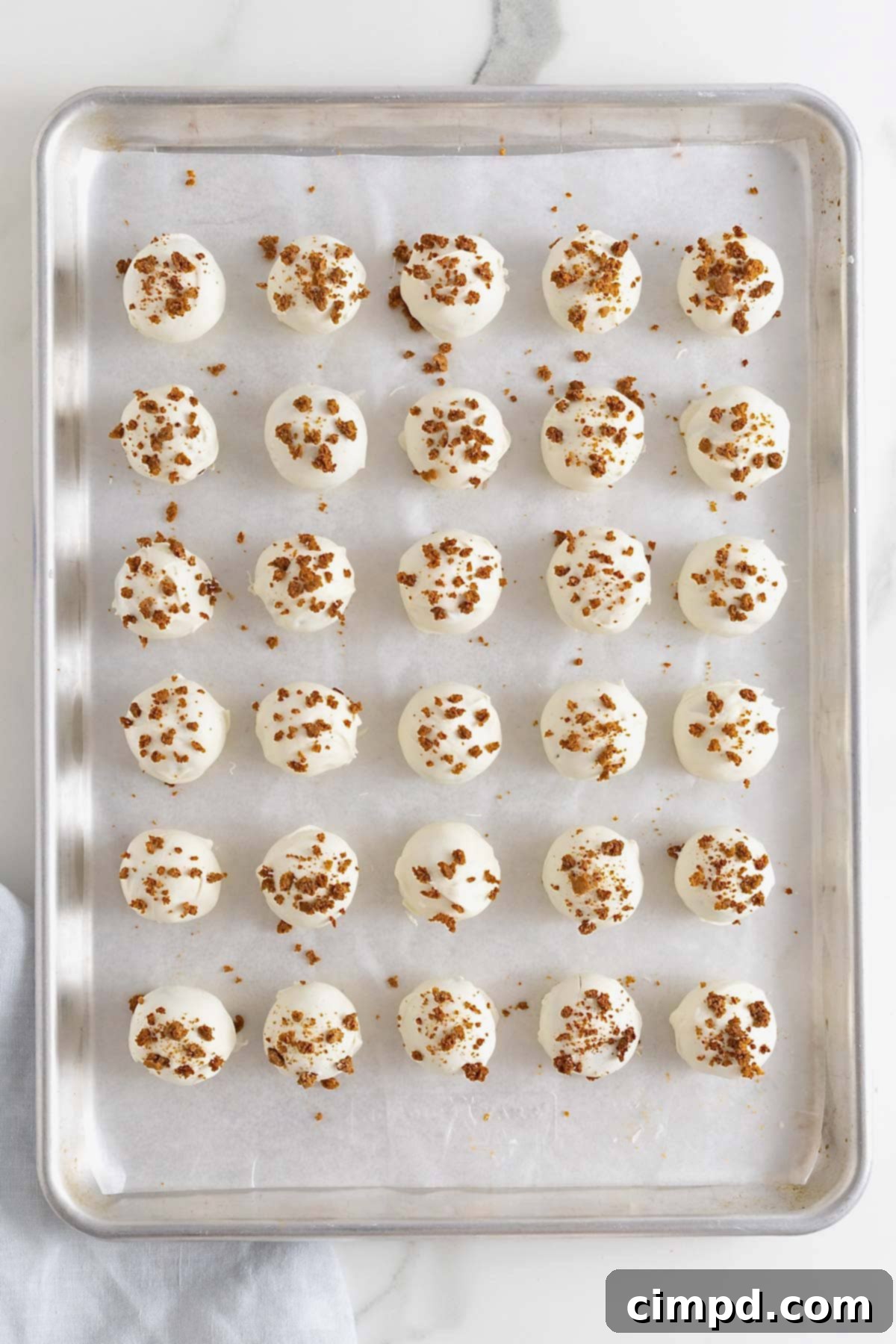 Rows of freshly coated pumpkin cake balls, adorned with sprinkles, neatly arranged on a parchment-covered aluminum baking sheet, cooling.