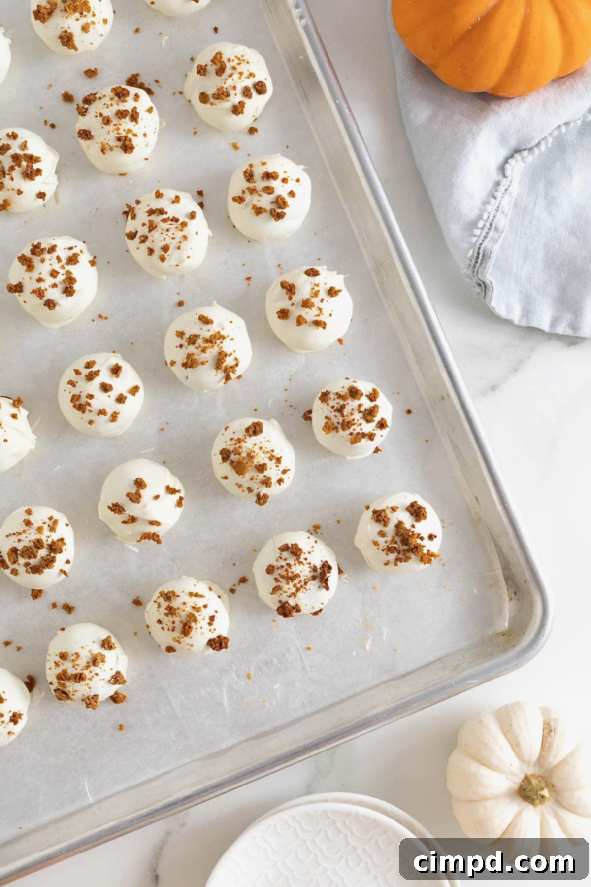 A closer view of the pumpkin cake balls, each perfectly coated and decorated, resting on a parchment-covered aluminum baking sheet.