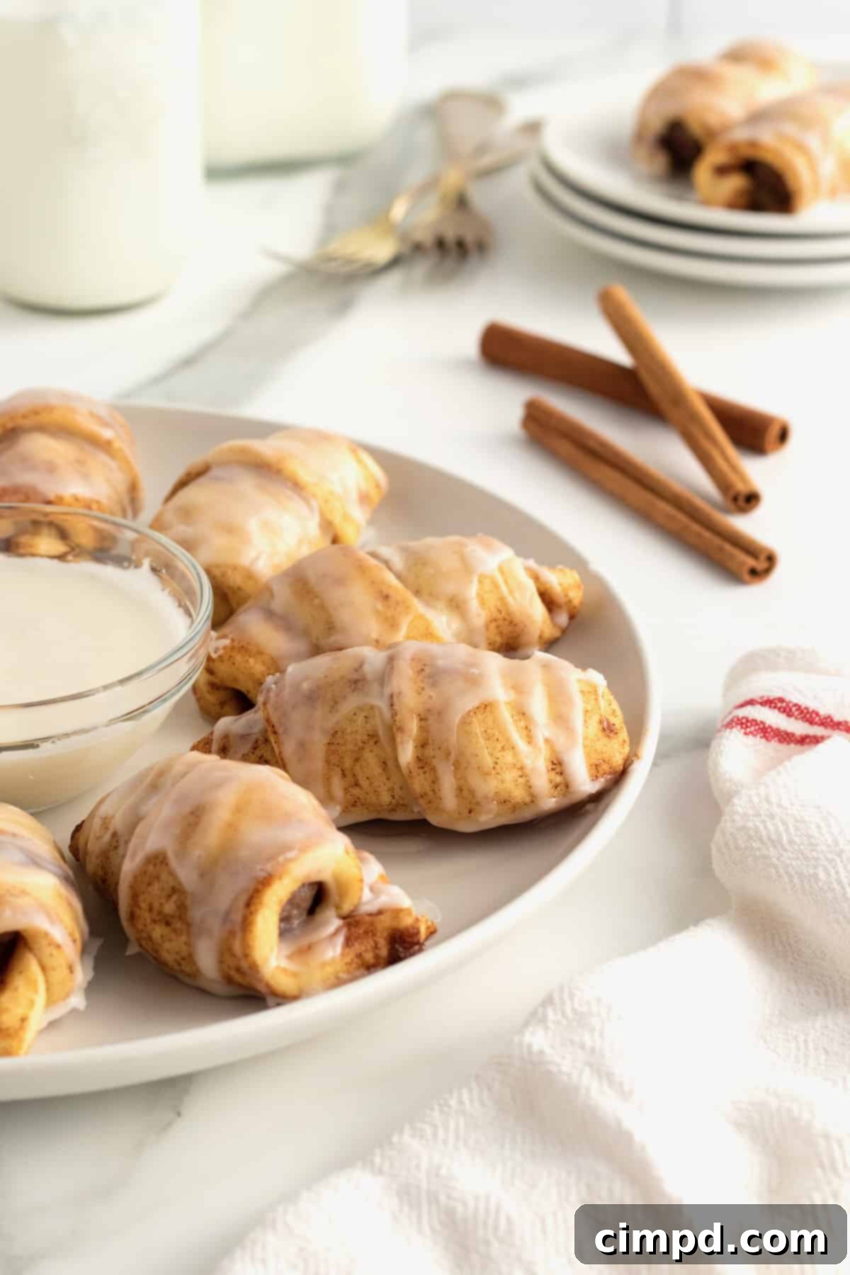 A beautifully arranged platter of finished Cinnamon Roll Pigs in a Blanket with a side of dipping icing.