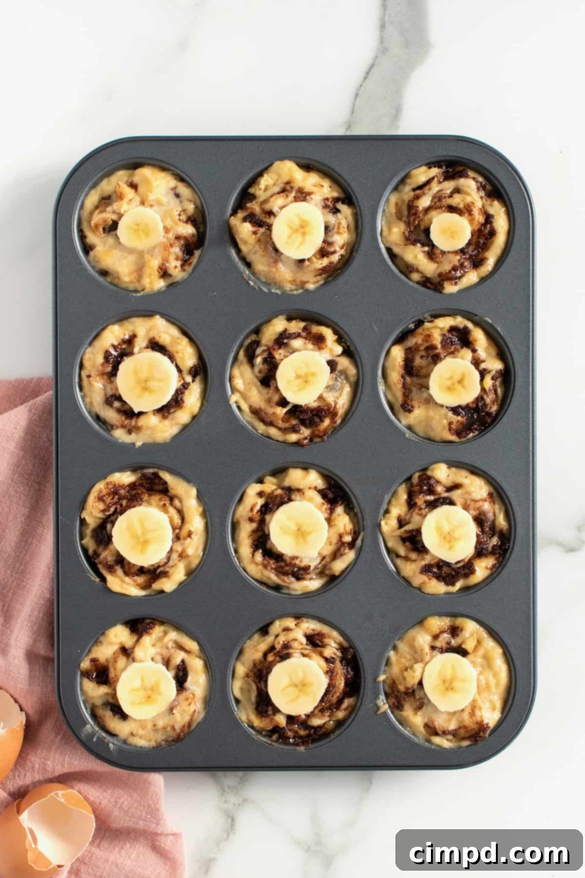Banana slices placed on top of swirled muffin batter