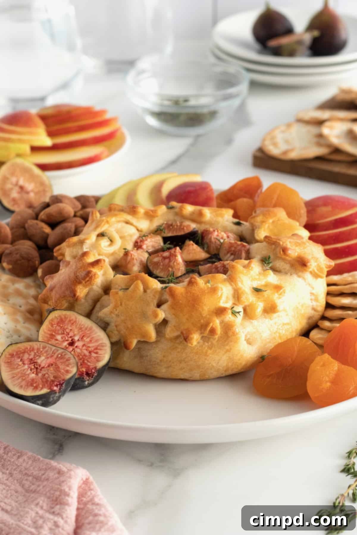 A large serving board filled with an assortment of crackers, fresh fruits, nuts, and a central baked brie with various toppings.