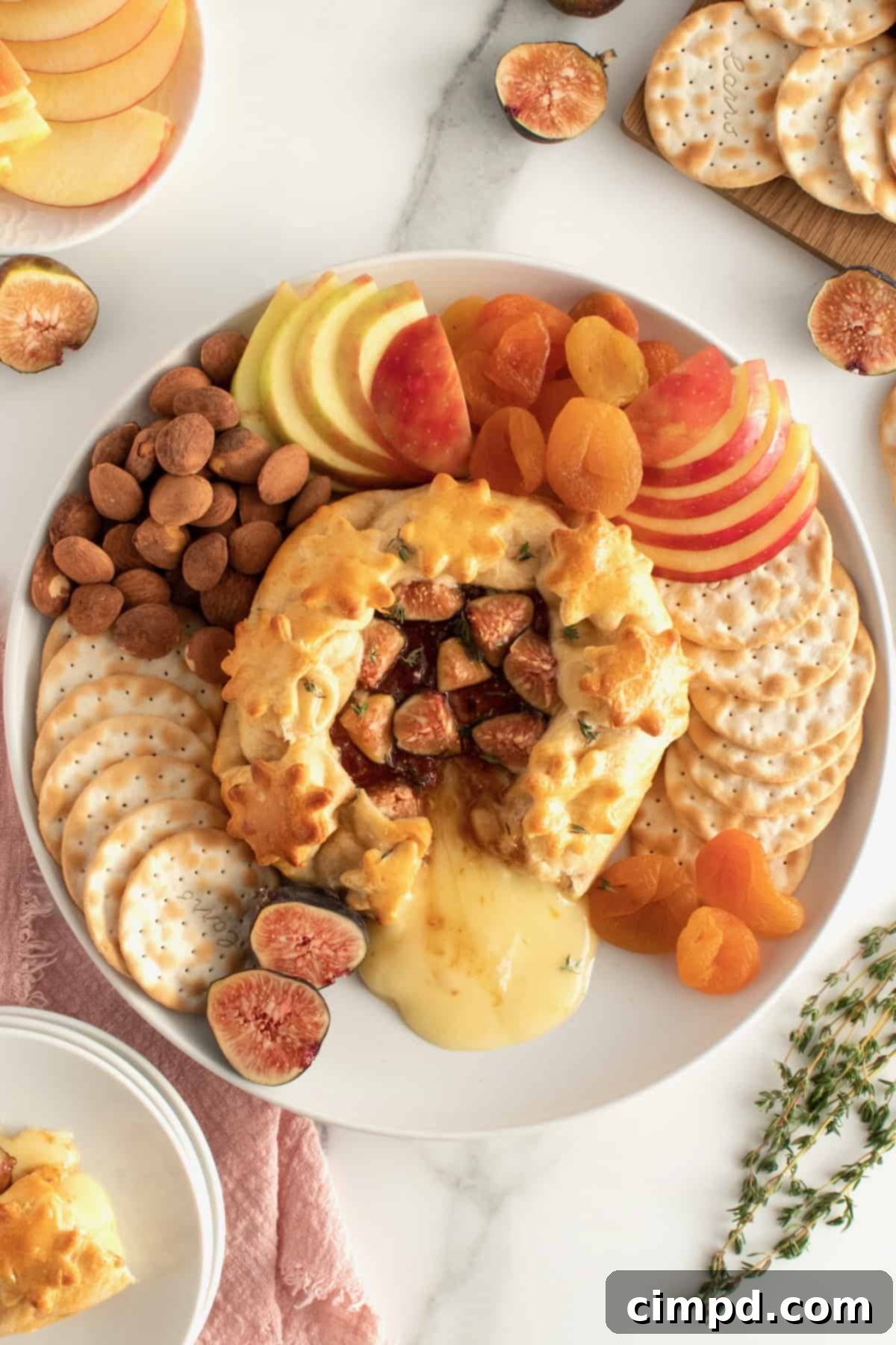 Baked Brie with Fig Jam on a serving platter surrounded by various crackers, nuts, and fruit, ready for guests.