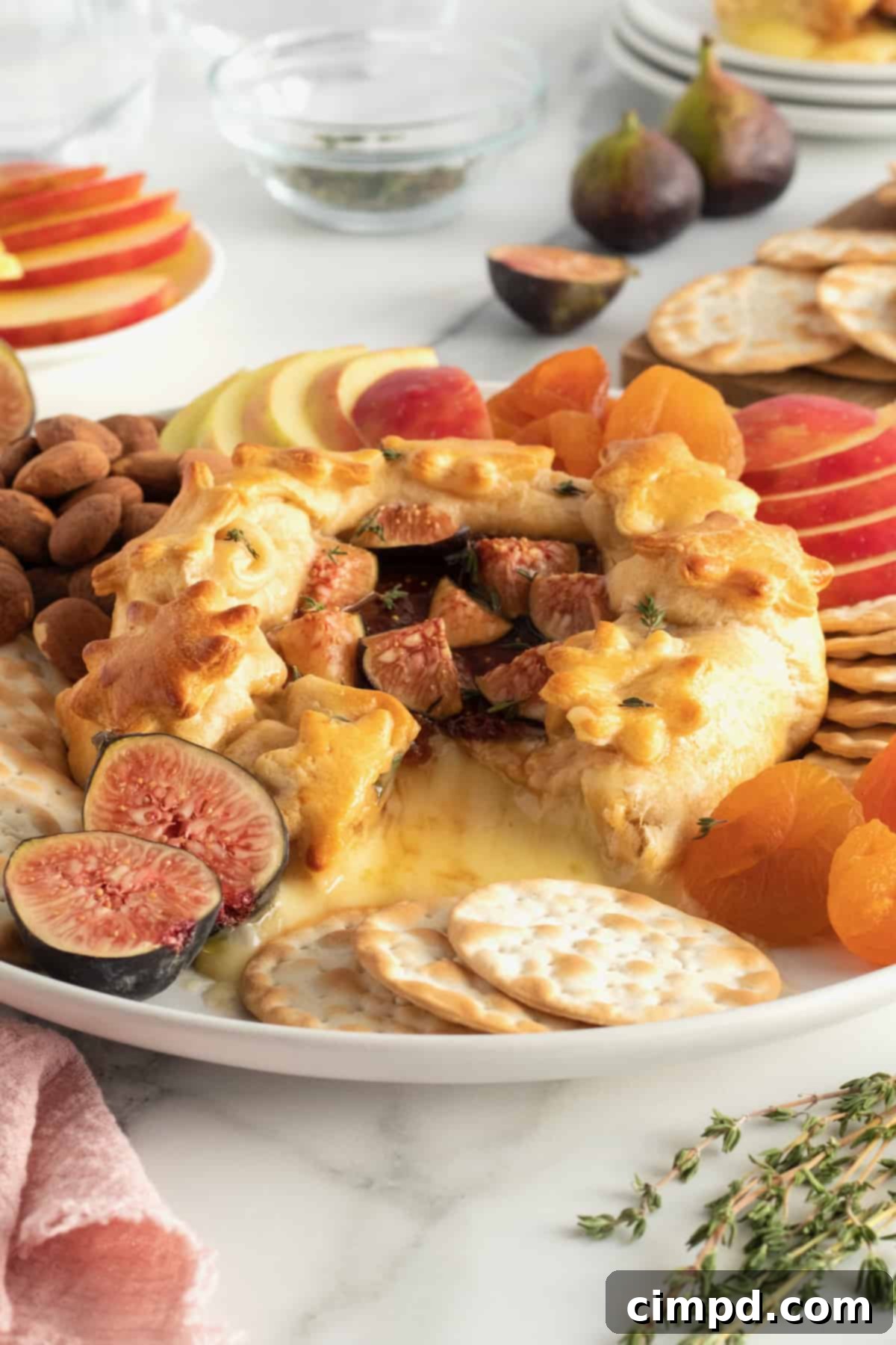 A slice of baked brie with fig jam on a small plate, showing the gooey cheese and flaky crust, garnished with a thyme sprig.