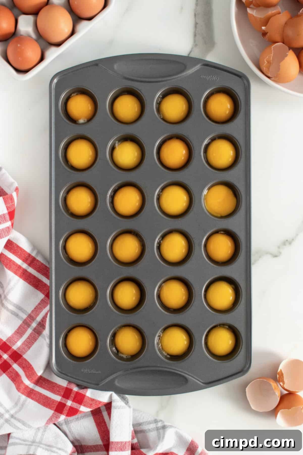 Bake Perfect Runny Eggs in Your Mini Muffin Pan 7 Separated egg yolks carefully placed into each cup of a mini muffin pan by The BakerMama