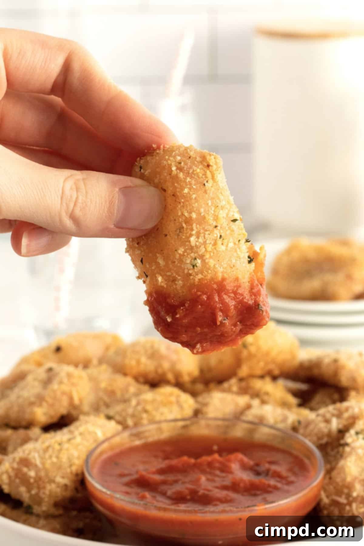Close-up of a hand dipping a crispy pepperoni pizza pocket bite into marinara sauce.