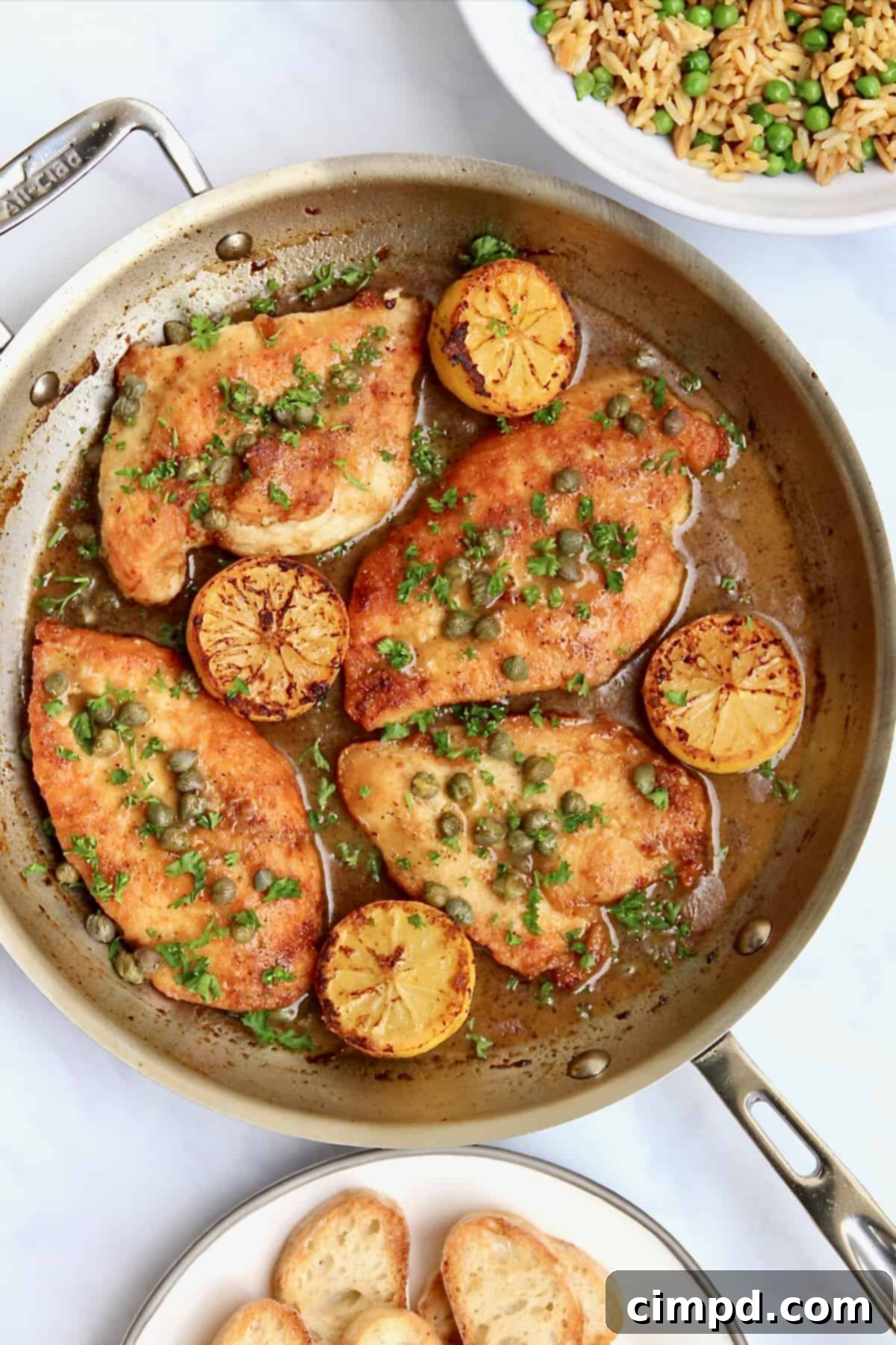 Whip Up Warmth: Speedy Suppers 3 Golden-brown chicken breasts in a skillet with lemon slices and capers, accompanied by a side of brown rice and green peas, and toasted baguette slices.