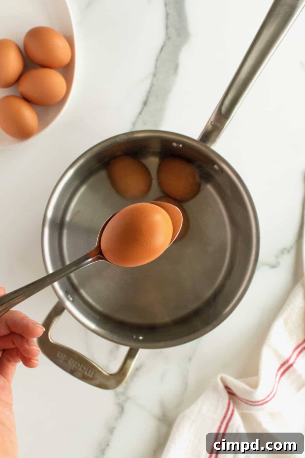 Lowering cold eggs into boiling water with a slotted spoon for soft boiling