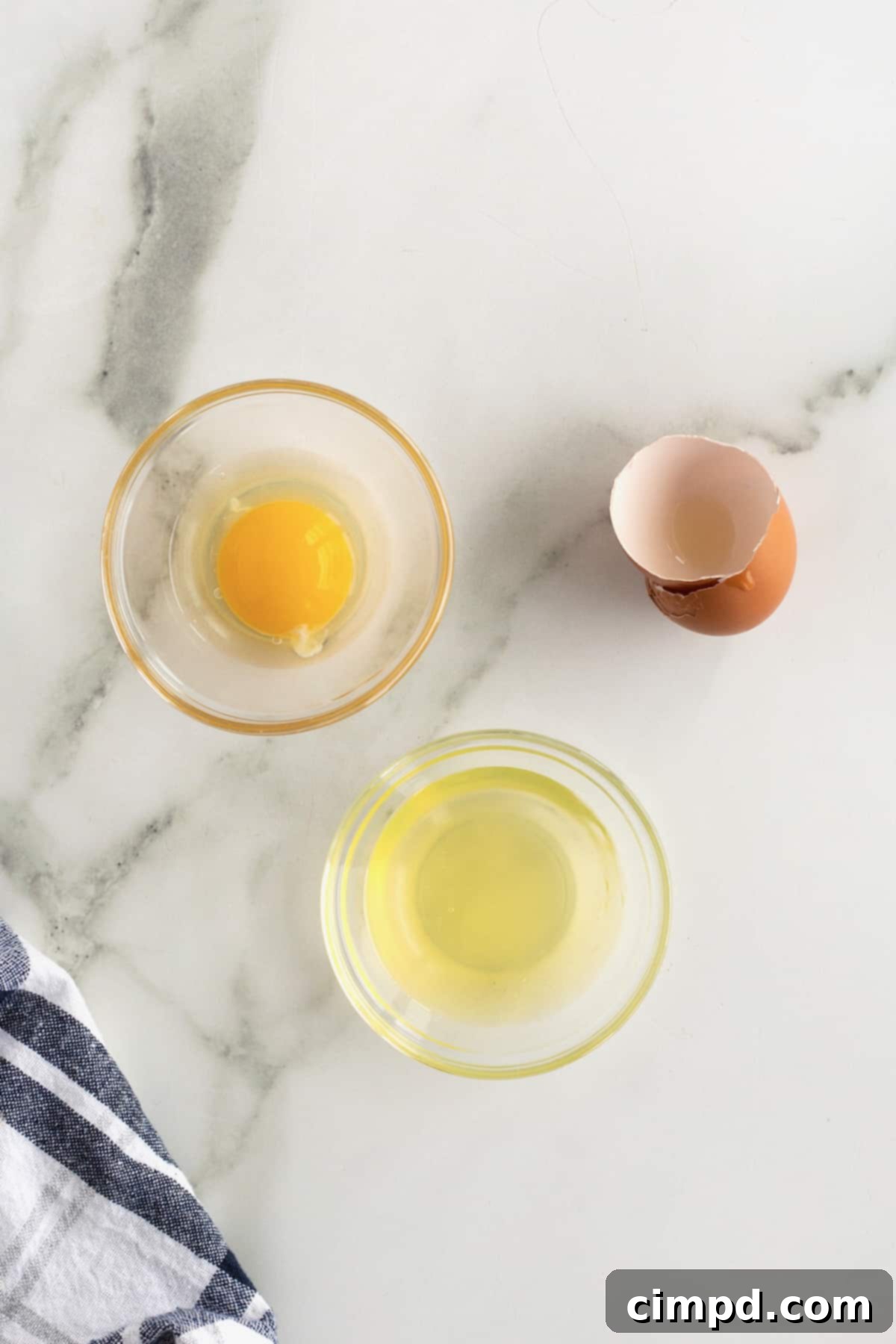 Flawless Egg Division 3 Expertly separated egg yolk in a shell, ready for a recipe, next to a bowl of clean egg whites, demonstrating a key culinary technique from The BakerMama.