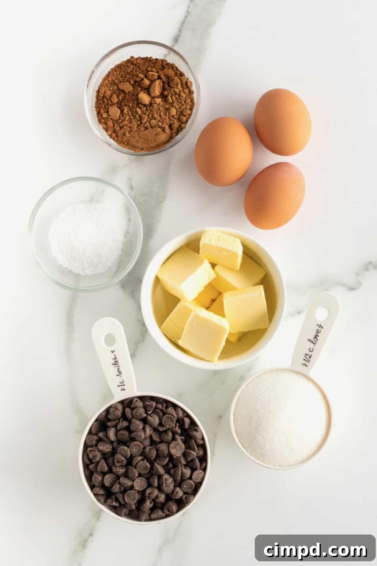 Key ingredients for Flourless Fudge Brownie Bites laid out: butter, chocolate chips, sugar, eggs, cocoa powder, and sea salt