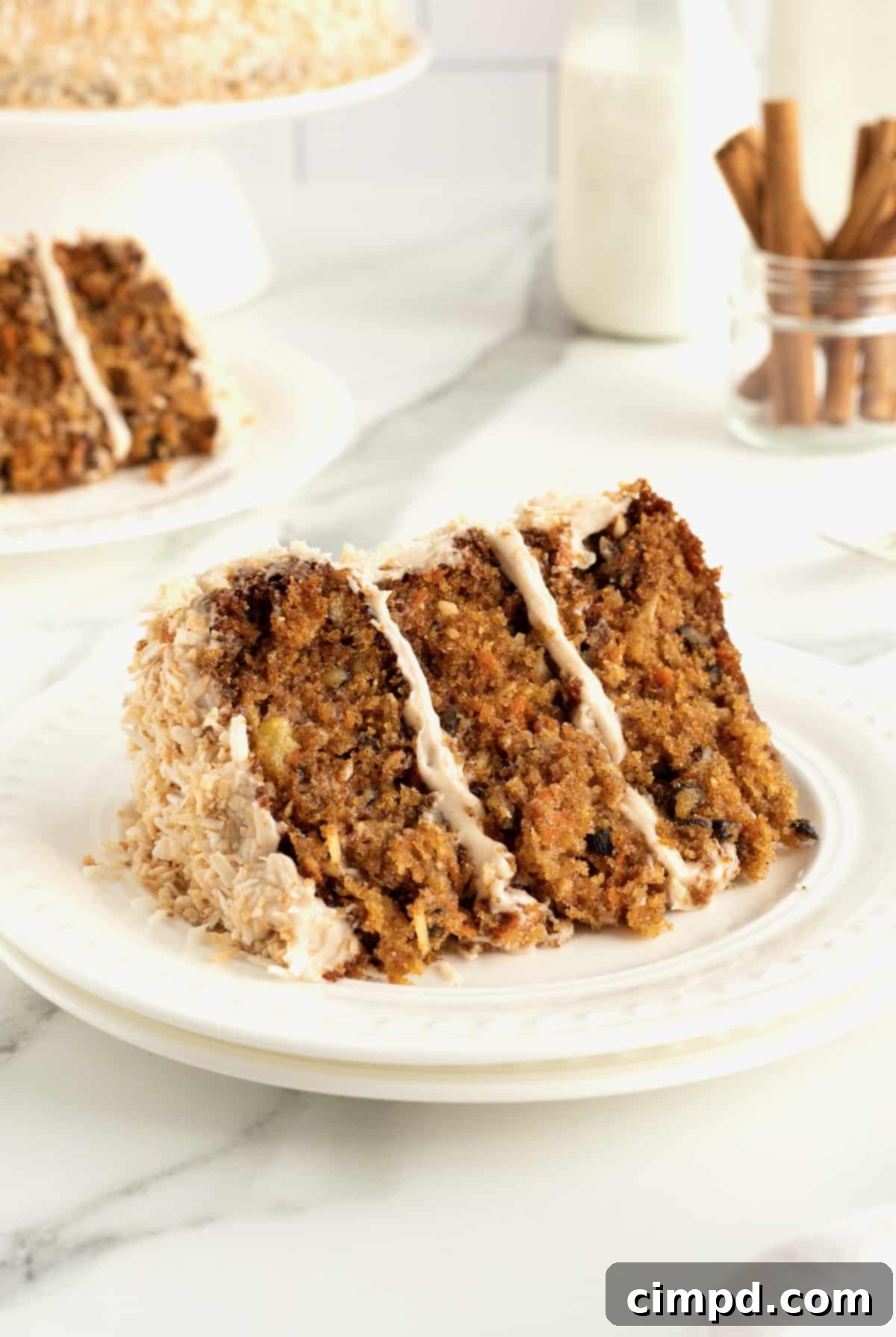 A stunning Coconut Carrot Cake adorned with a generous layer of Cinnamon Cream Cheese Frosting, presented elegantly by The BakerMama.