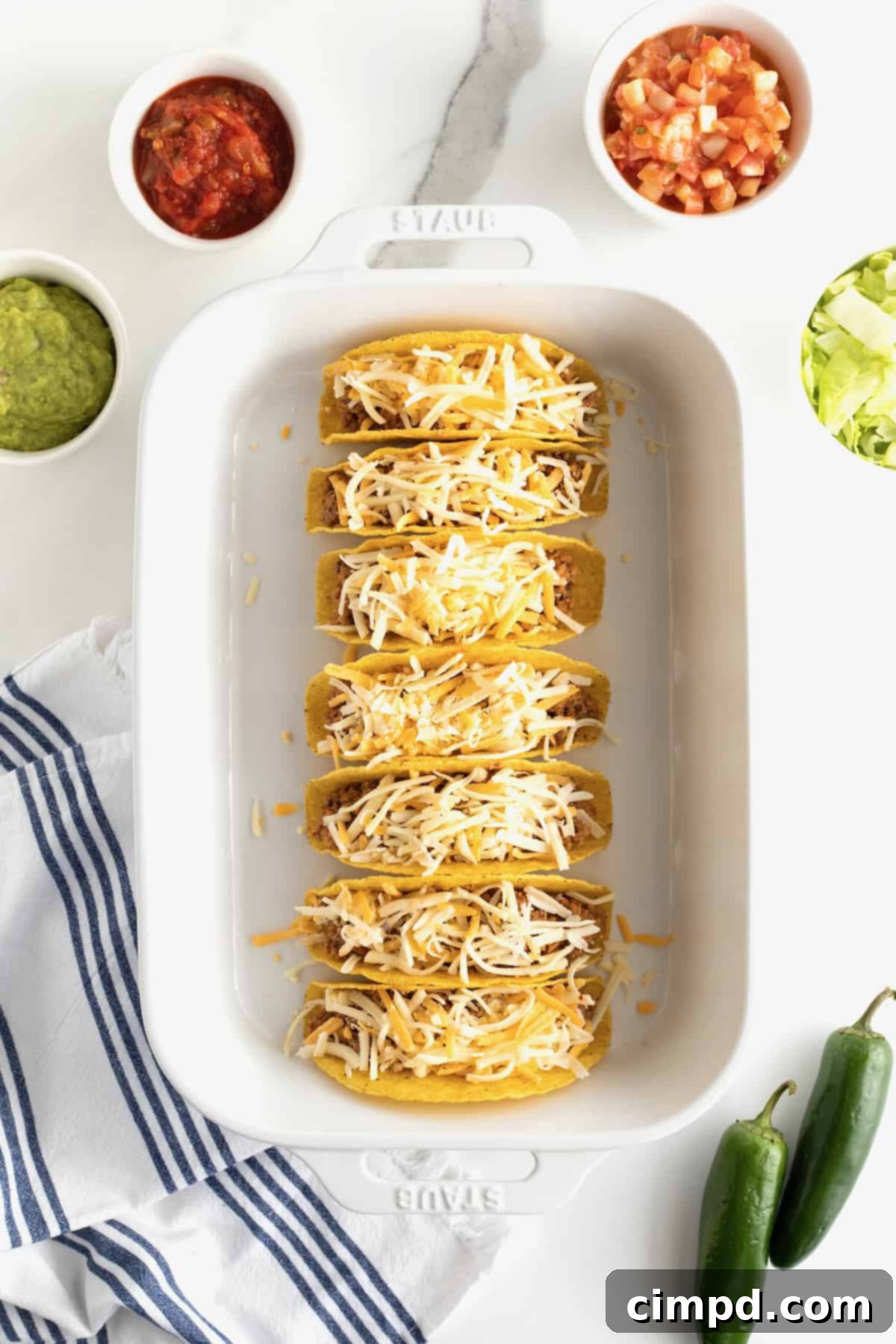 Beef and Bean Baked Tacos in a baking dish, topped with shredded cheese, ready for the oven, by The BakerMama