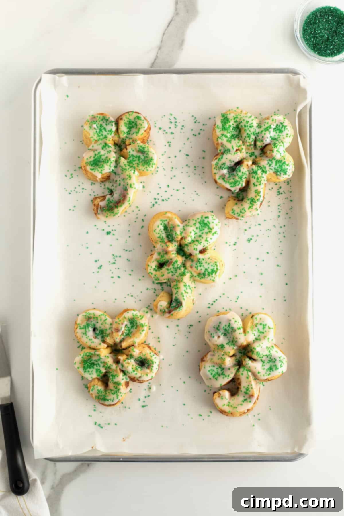 Finished St. Patrick's Day Cinnamon Rolls being adorned with green sugar sprinkles