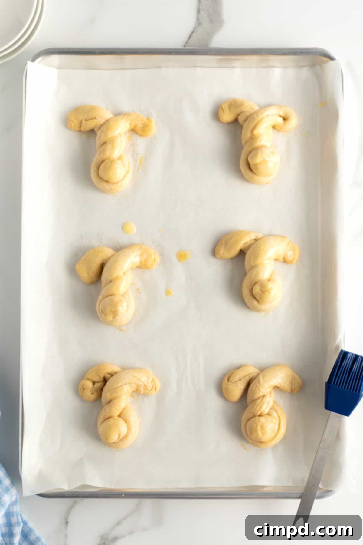 Fluffy Bunny Crescent Rolls 9 Freshly baked golden brown bunny shaped crescent dinner rolls on a baking sheet, glistening with melted butter
