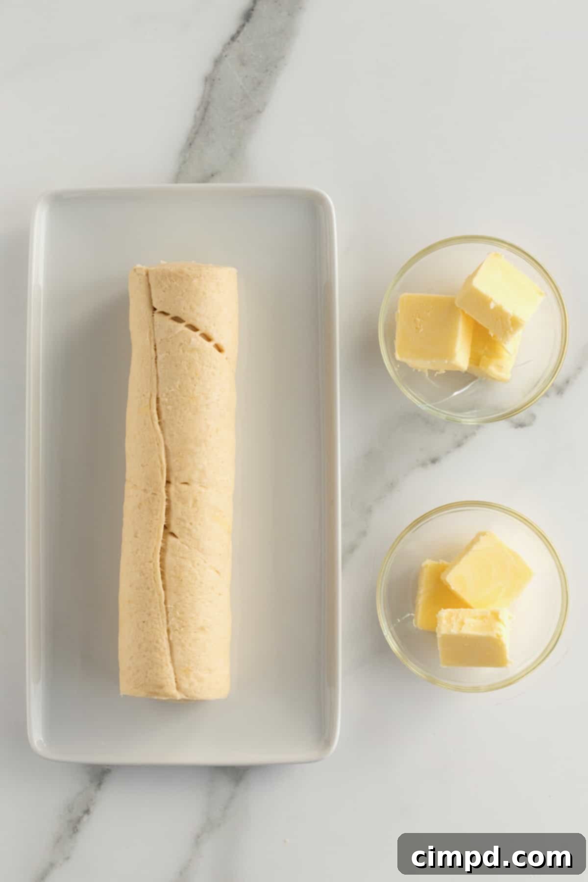 Fluffy Bunny Crescent Rolls 5 Ingredients laid out on a cutting board: a can of crescent rolls, a small bowl of melted butter, and a knife for preparation
