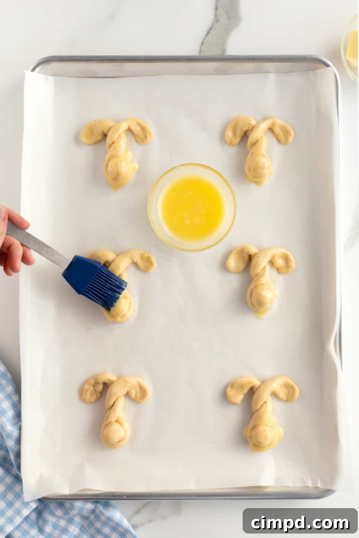 Fluffy Bunny Crescent Rolls 8 A hand brushing melted butter onto the raw bunny shaped crescent dough on a baking sheet