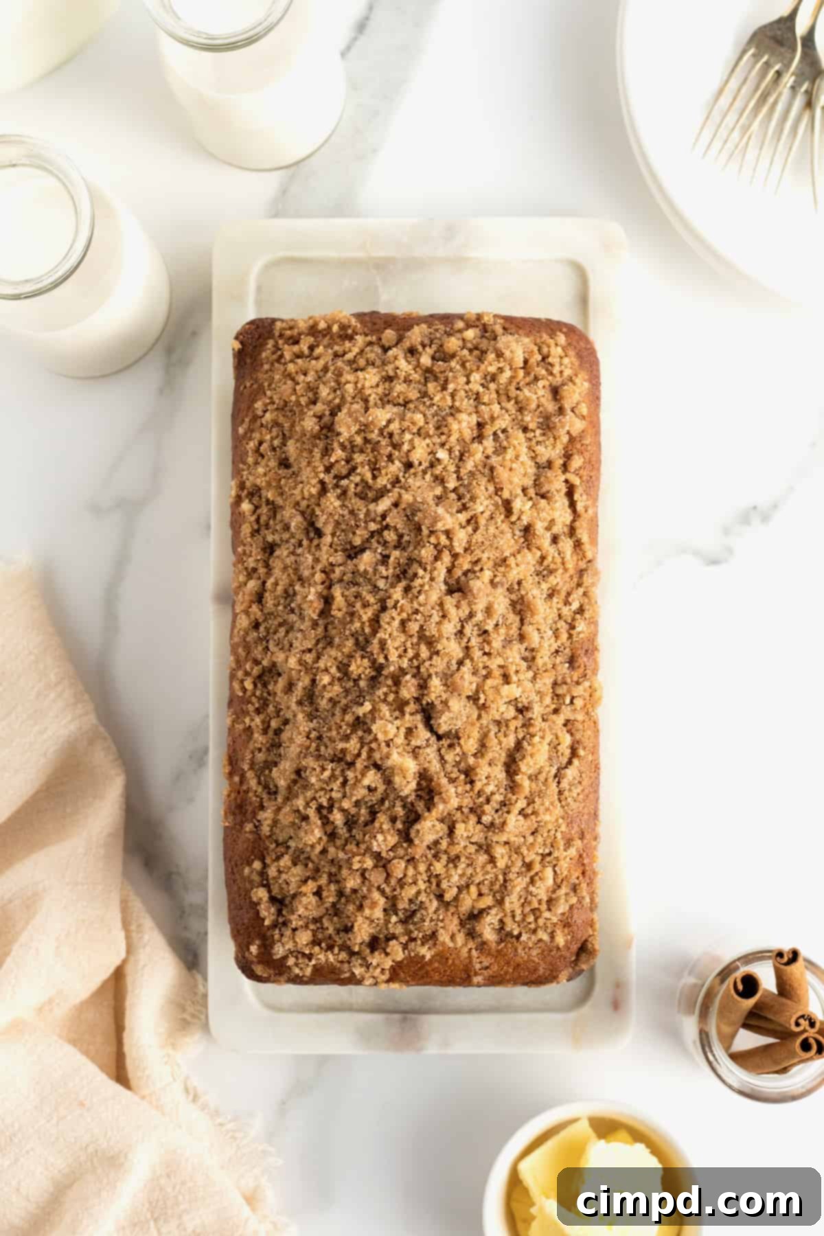 A whole loaf of Maple Cinnamon Streusel Bread on a wooden board, with a knife and a few slices already cut.