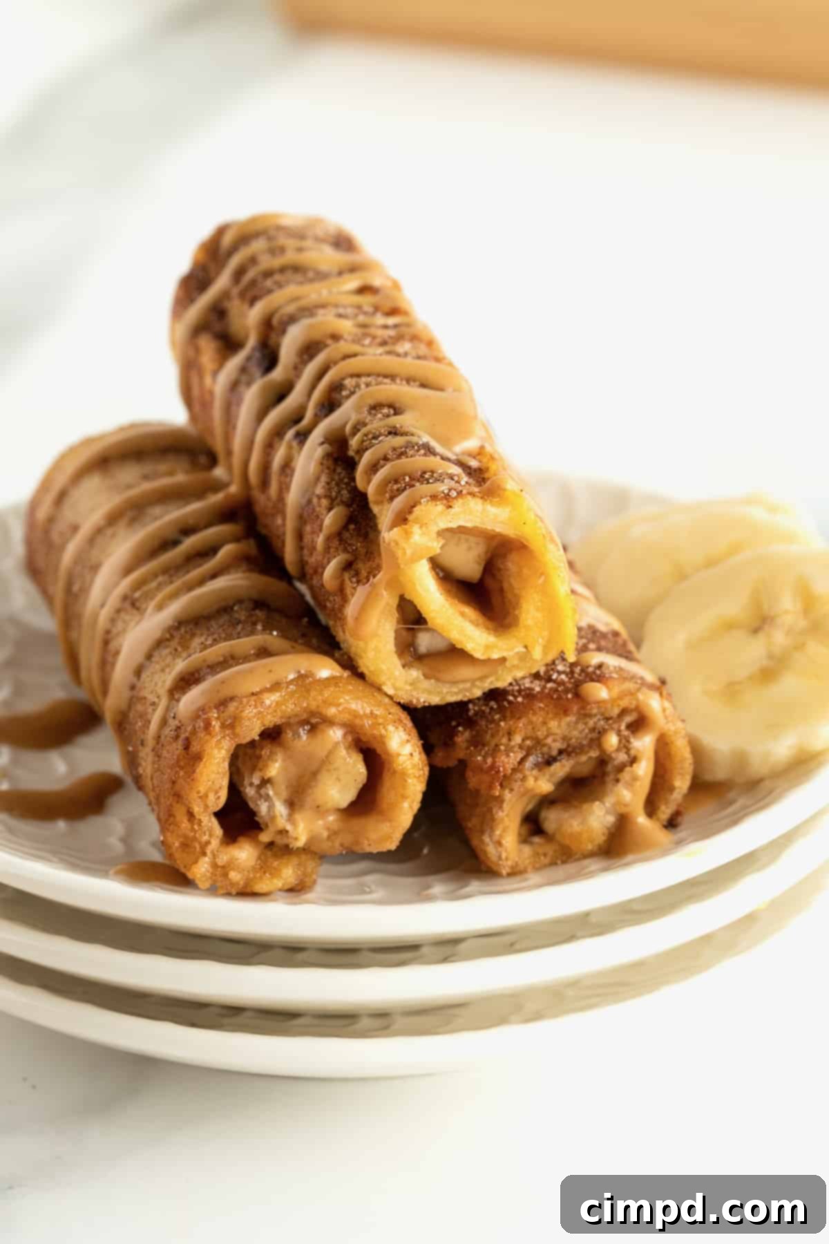 Golden brown Peanut Butter Banana French Toast Roll Ups on a serving platter, drizzled with melted peanut butter.