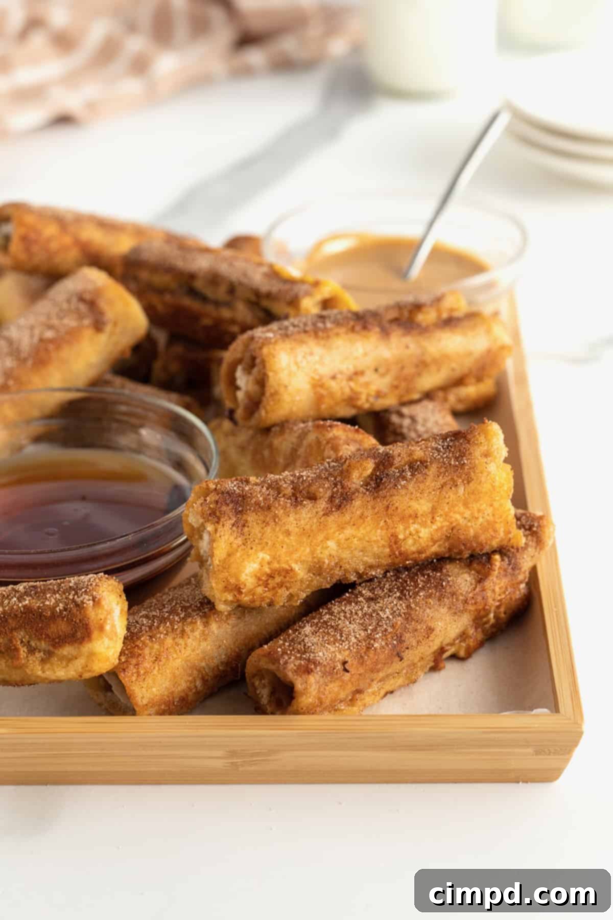 Peanut Butter Banana French Toast Roll Ups displayed with melted peanut butter drizzle and a side of maple syrup.