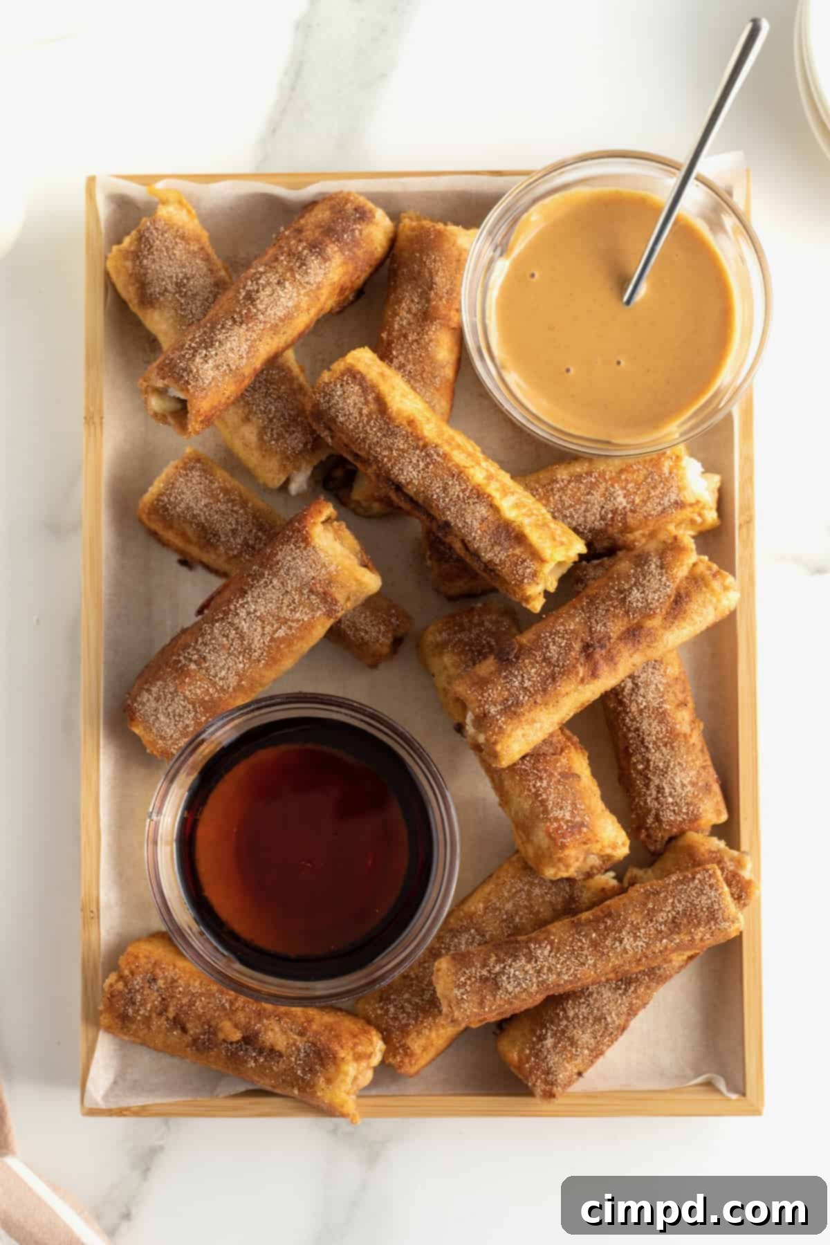 Peanut Butter Banana French Toast Roll Ups served on a wooden board with a small bowl of melted peanut butter.