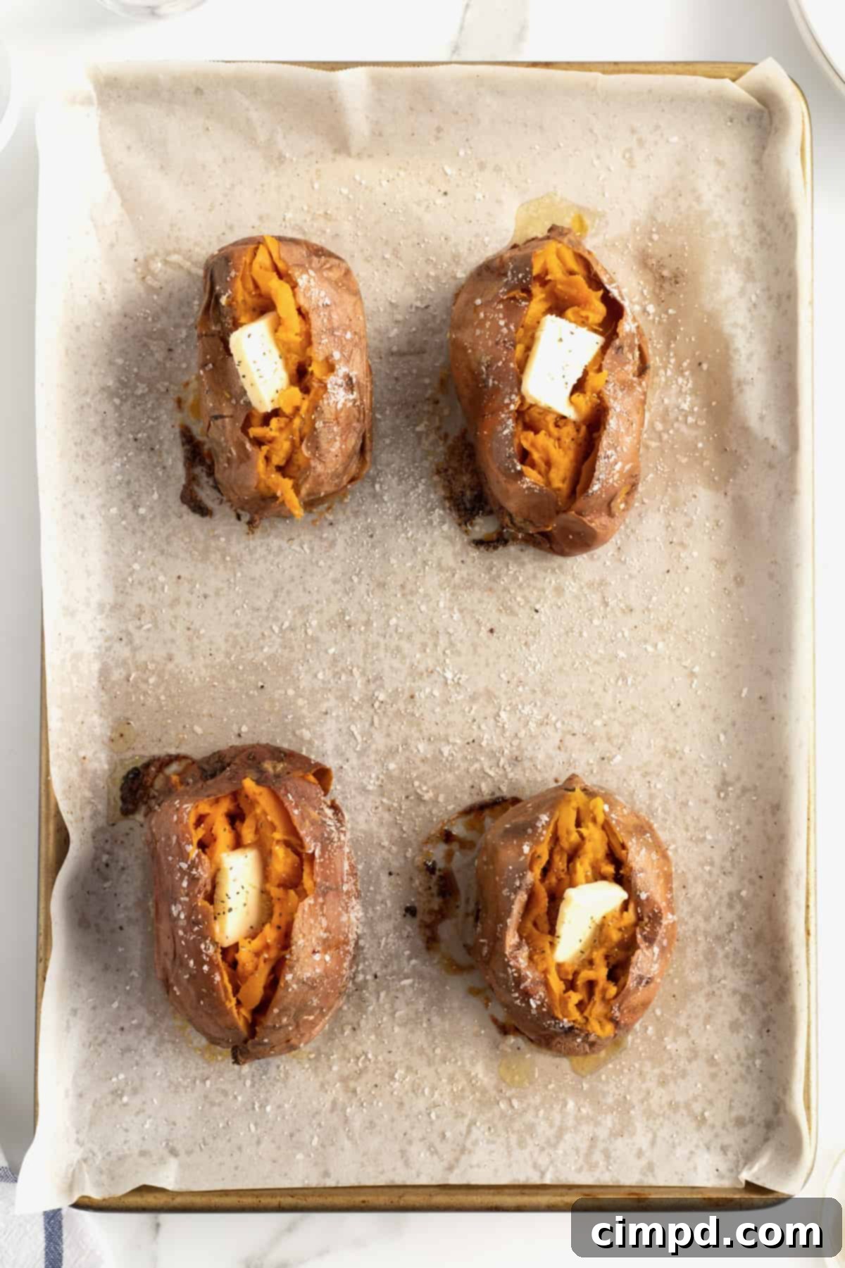 Perfect Baked Sweet Potatoes 11 Four sweet potatoes on a piece of parchment with salt sprinkled all around. The sweet potatoes are split open with a pat of butter inside.