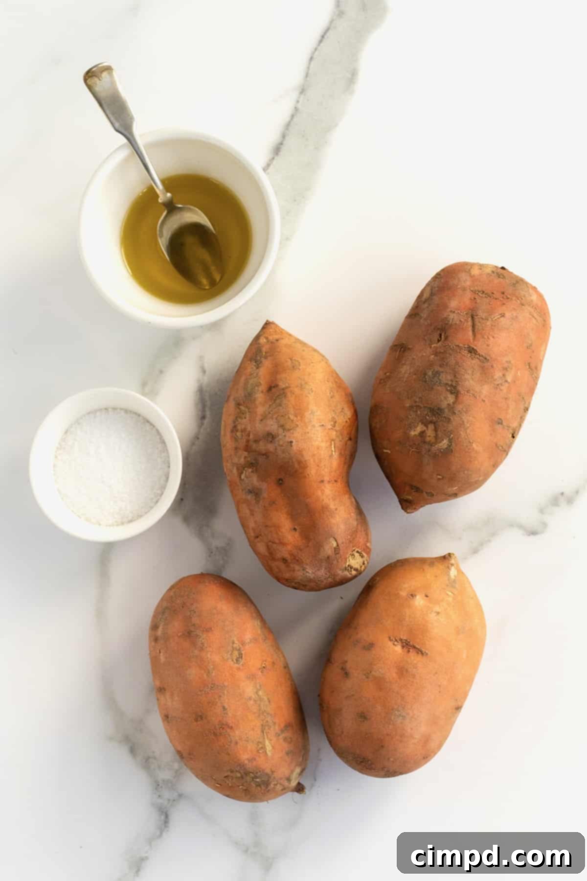 Perfect Baked Sweet Potatoes 7 A small dish of olive oil, a small dish of coarse salt, and four raw sweet potatoes on a white marble counter.