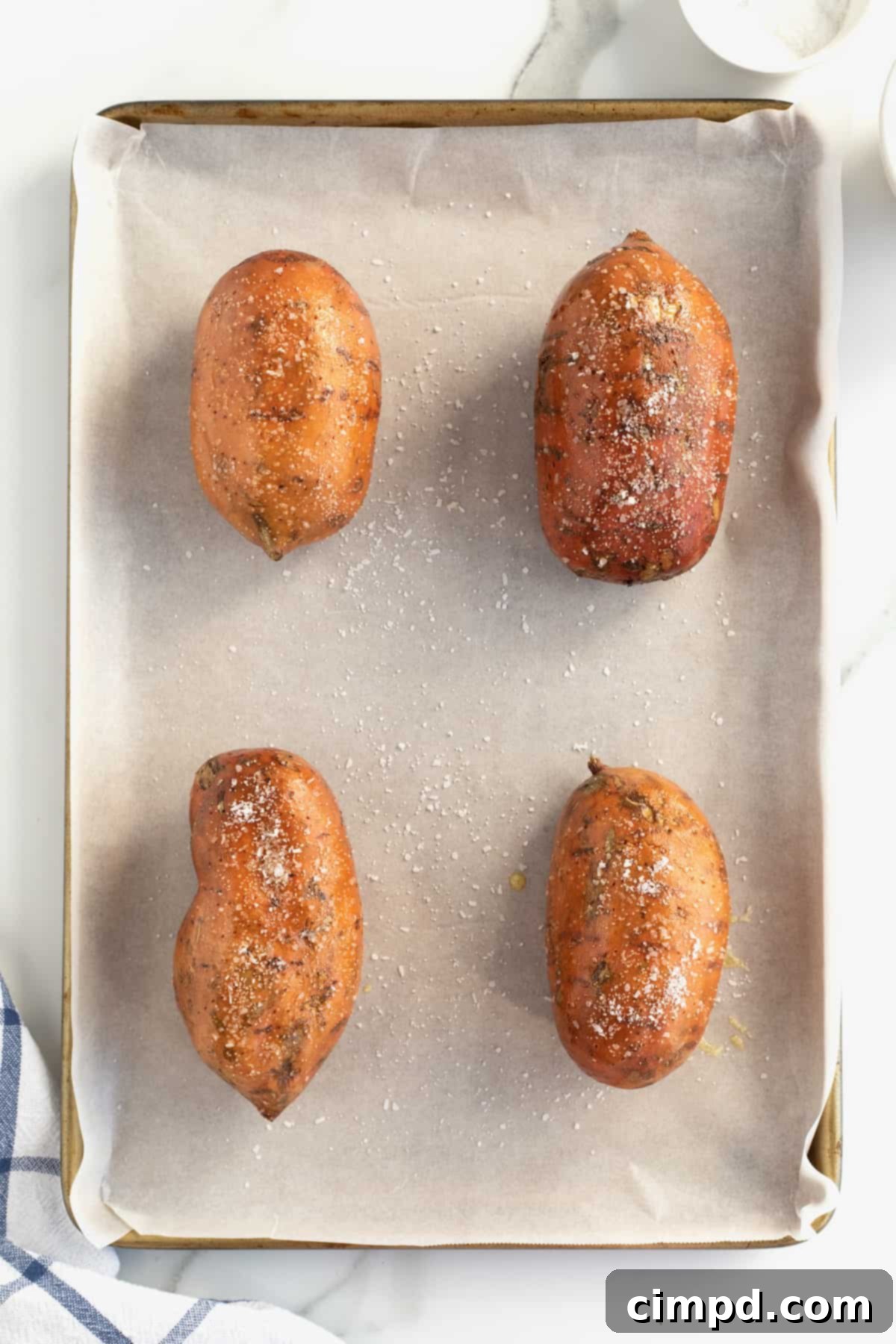 Perfect Baked Sweet Potatoes 9 Four raw sweet potatoes on a parchment lined baking sheet, generously sprinkled with salt.