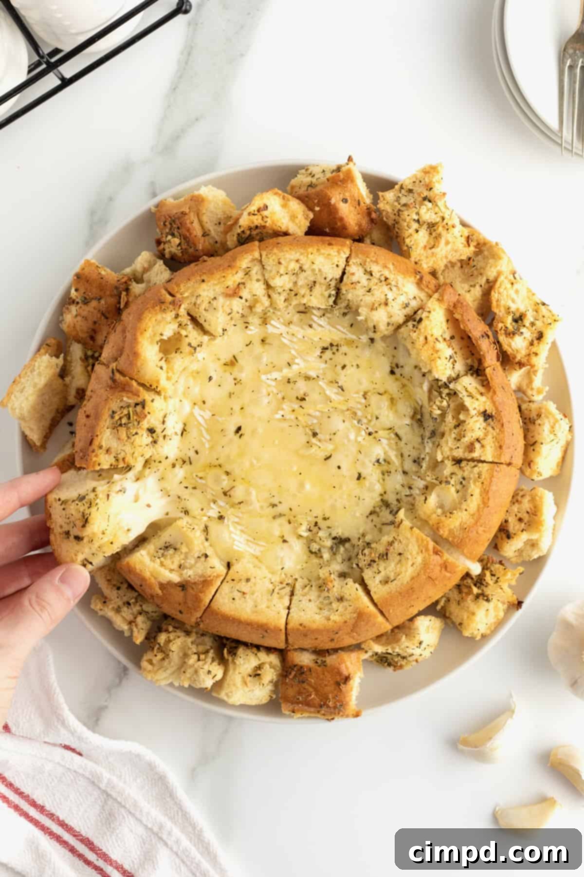 Melted brie in a sourdough bread bowl on a white ceramic serving plate.