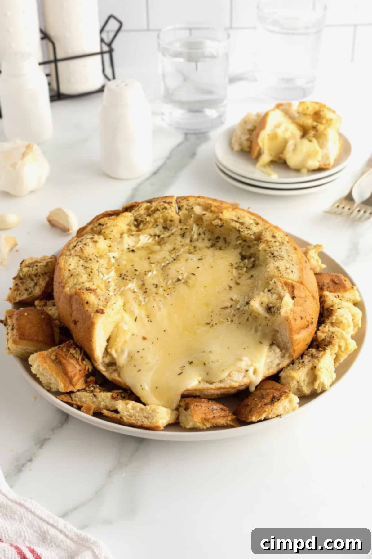 Baked brie melting out of a sourdough bread bowl on a white ceramic serving plate.