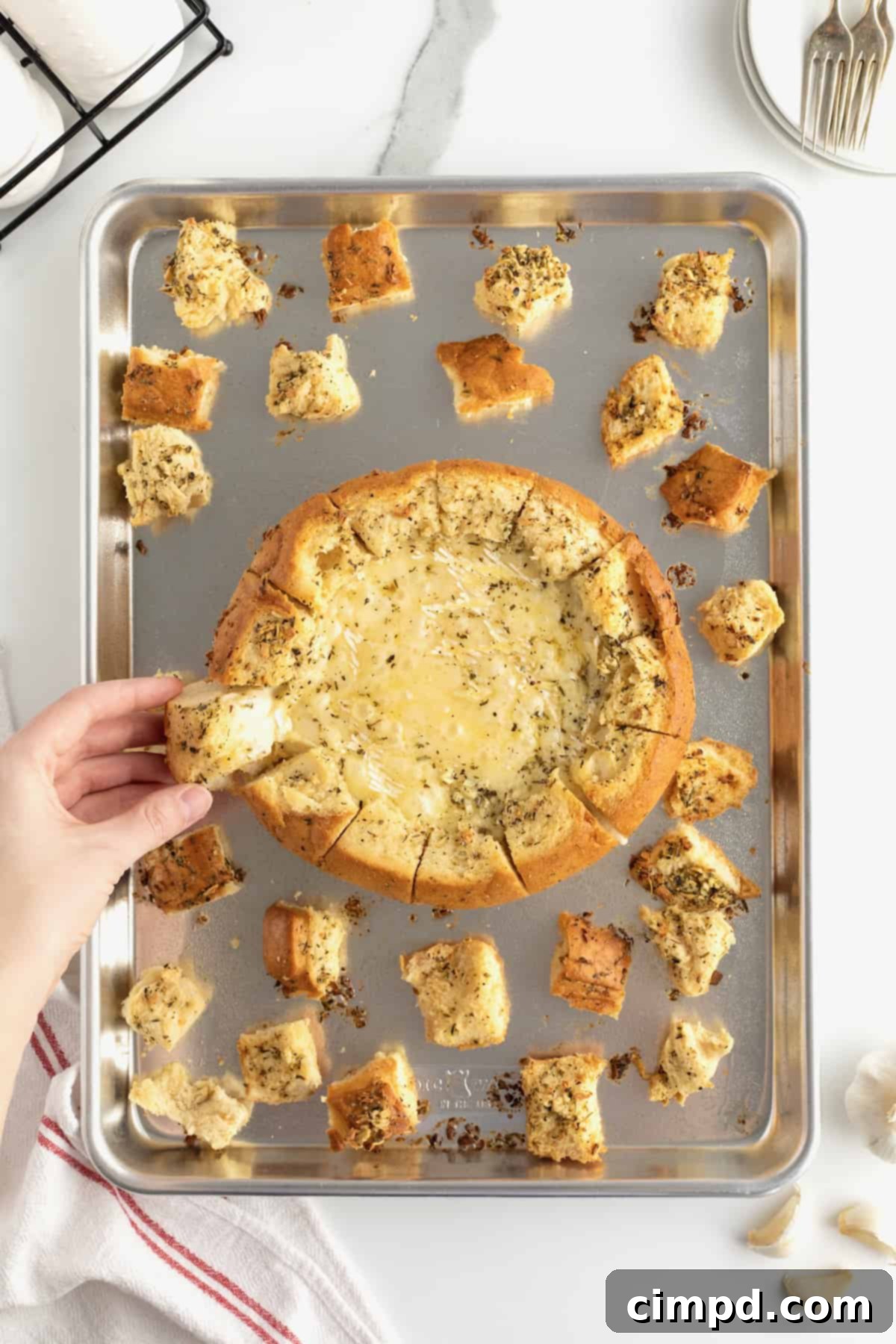 Bread bowl with wheel of brie inside arranged on baking sheet with bread chunks.