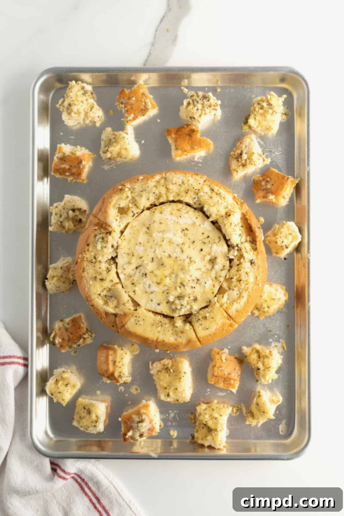 Bread bowl with wheel of brie inside arranged on baking sheet with bread chunks.