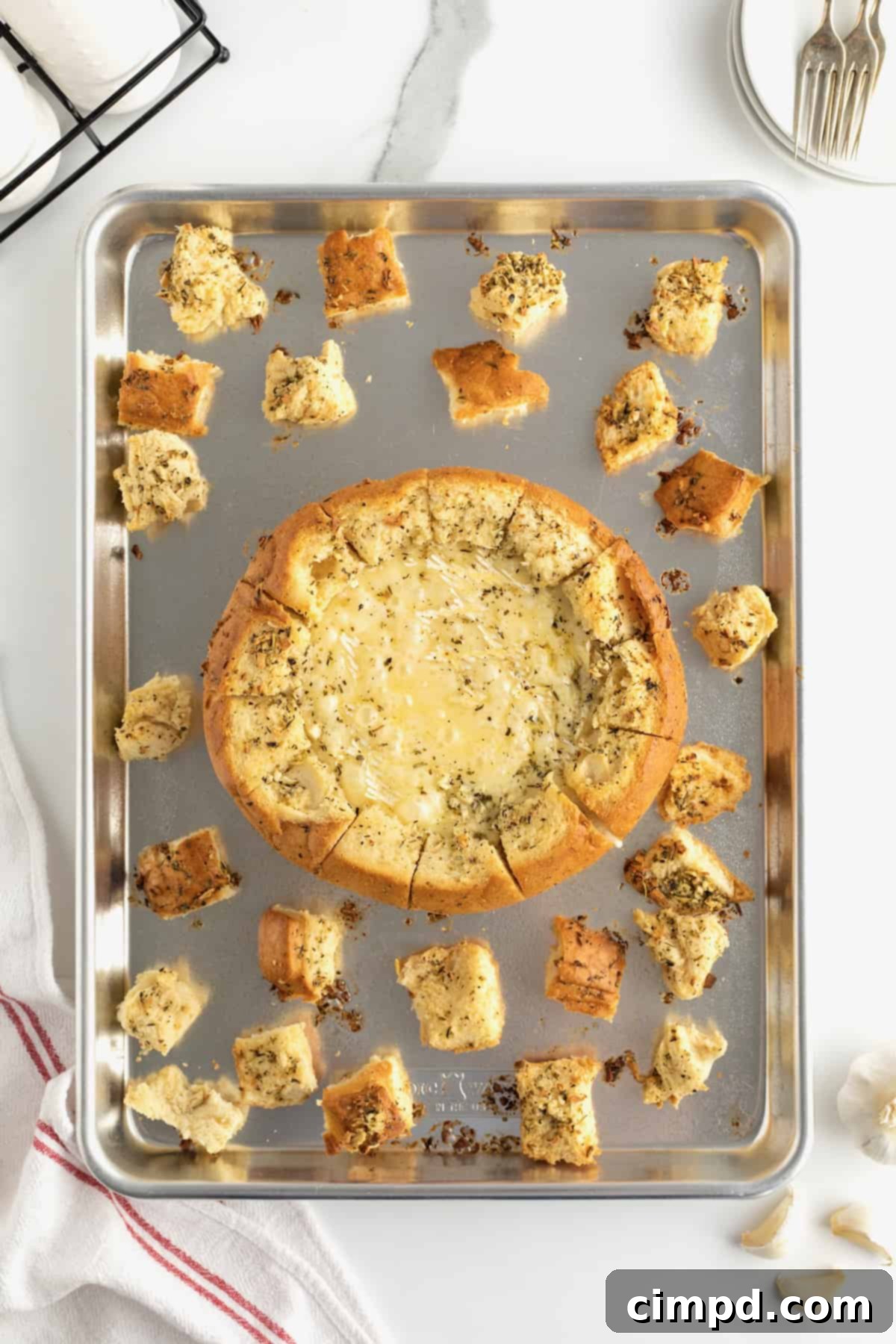 A baked bread bowl with wheel of brie inside arranged on baking sheet with bread chunks.