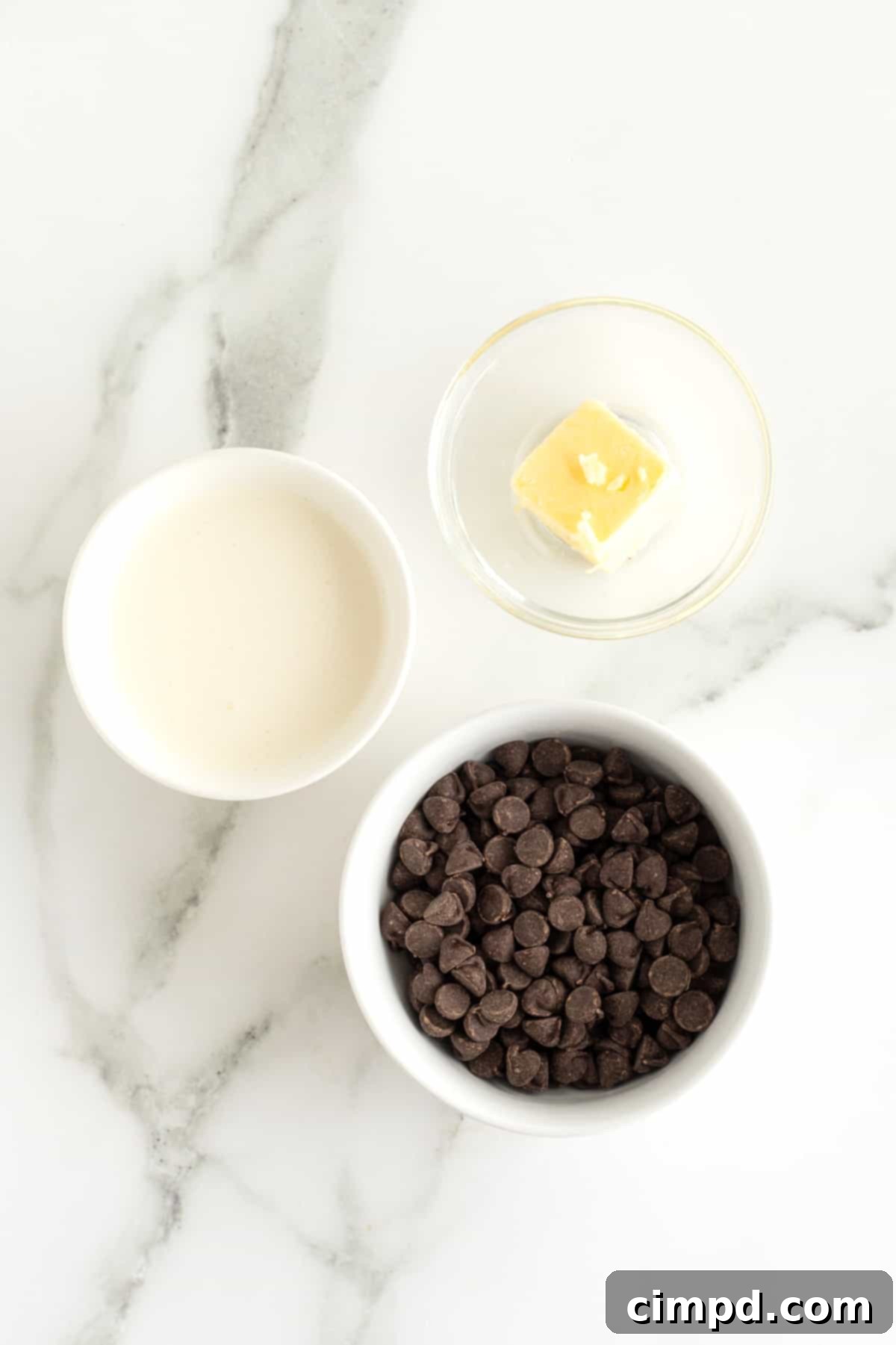 A close-up shot of the initial ingredients for chocolate ganache: a clear glass bowl filled with semi-sweet chocolate chips and a knob of unsalted butter, ready for the microwave.