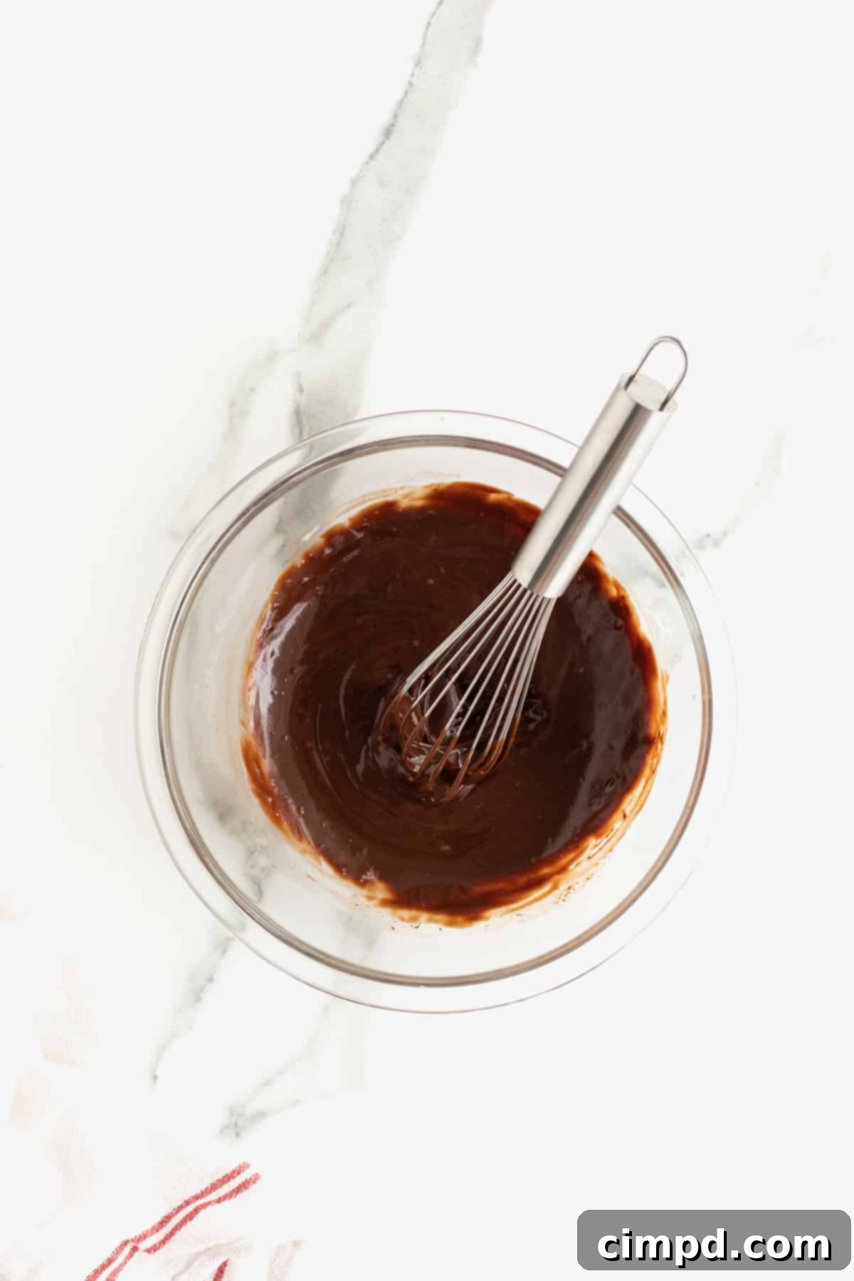 Perfectly whisked chocolate ganache in a clear glass bowl, featuring a smooth and glossy texture, ready for use. A metal whisk rests just outside the bowl, indicating a finished masterpiece.