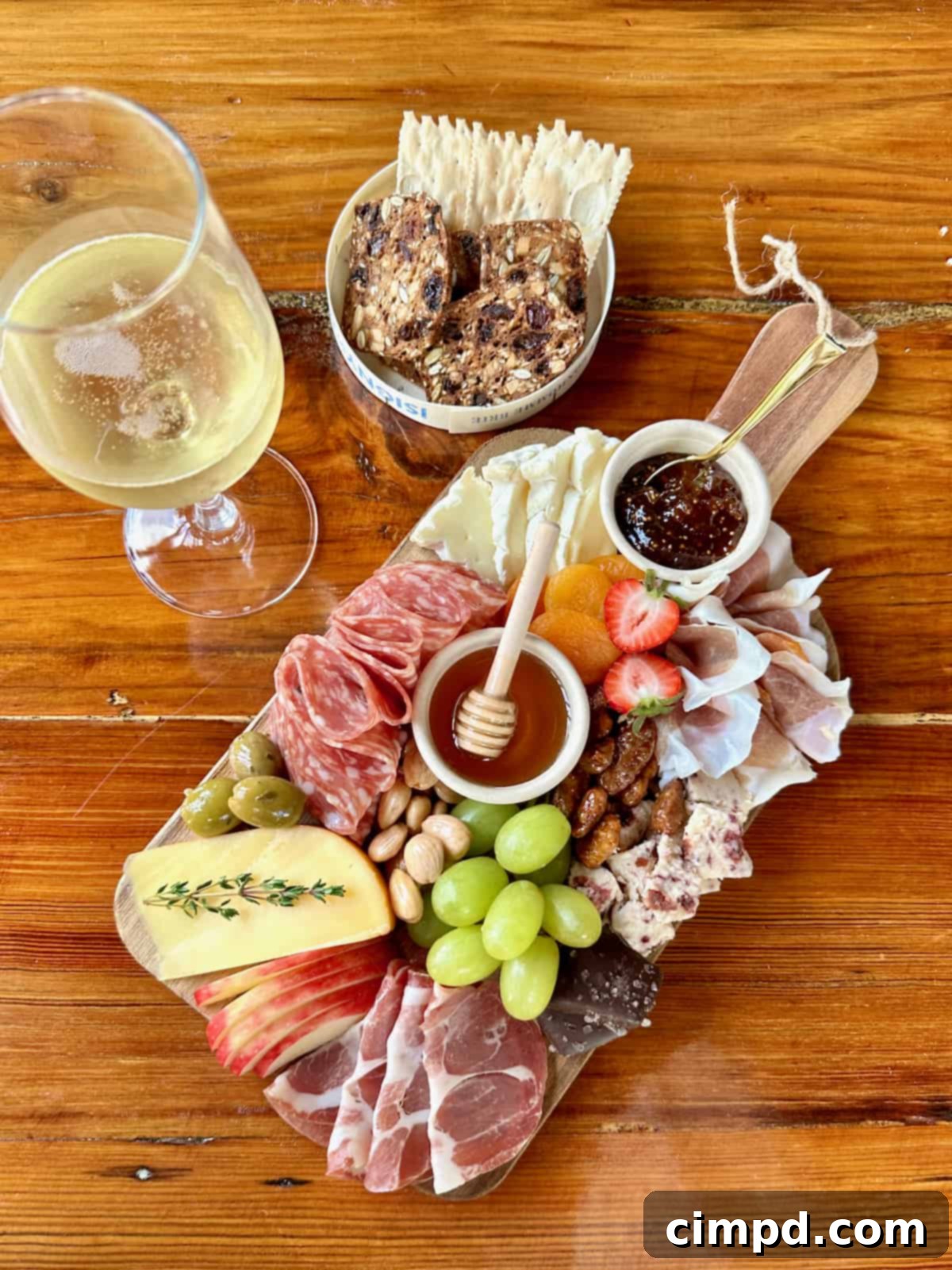 A beautifully arranged natural wood serving board with fresh green grapes, crisp apple slices, golden honey with a dipper, all positioned beside a refreshing glass of white wine.